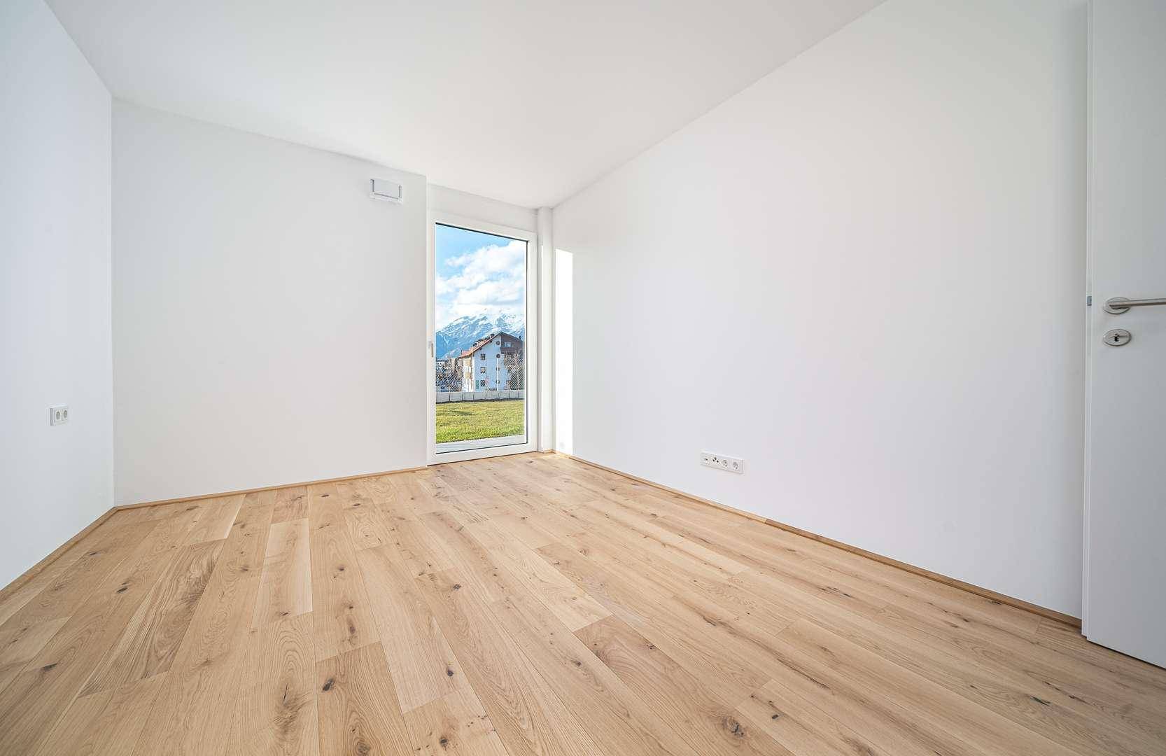 Helles Zimmer mit Holzboden und bodentiefem Fenster, das einen Bergblick bietet.