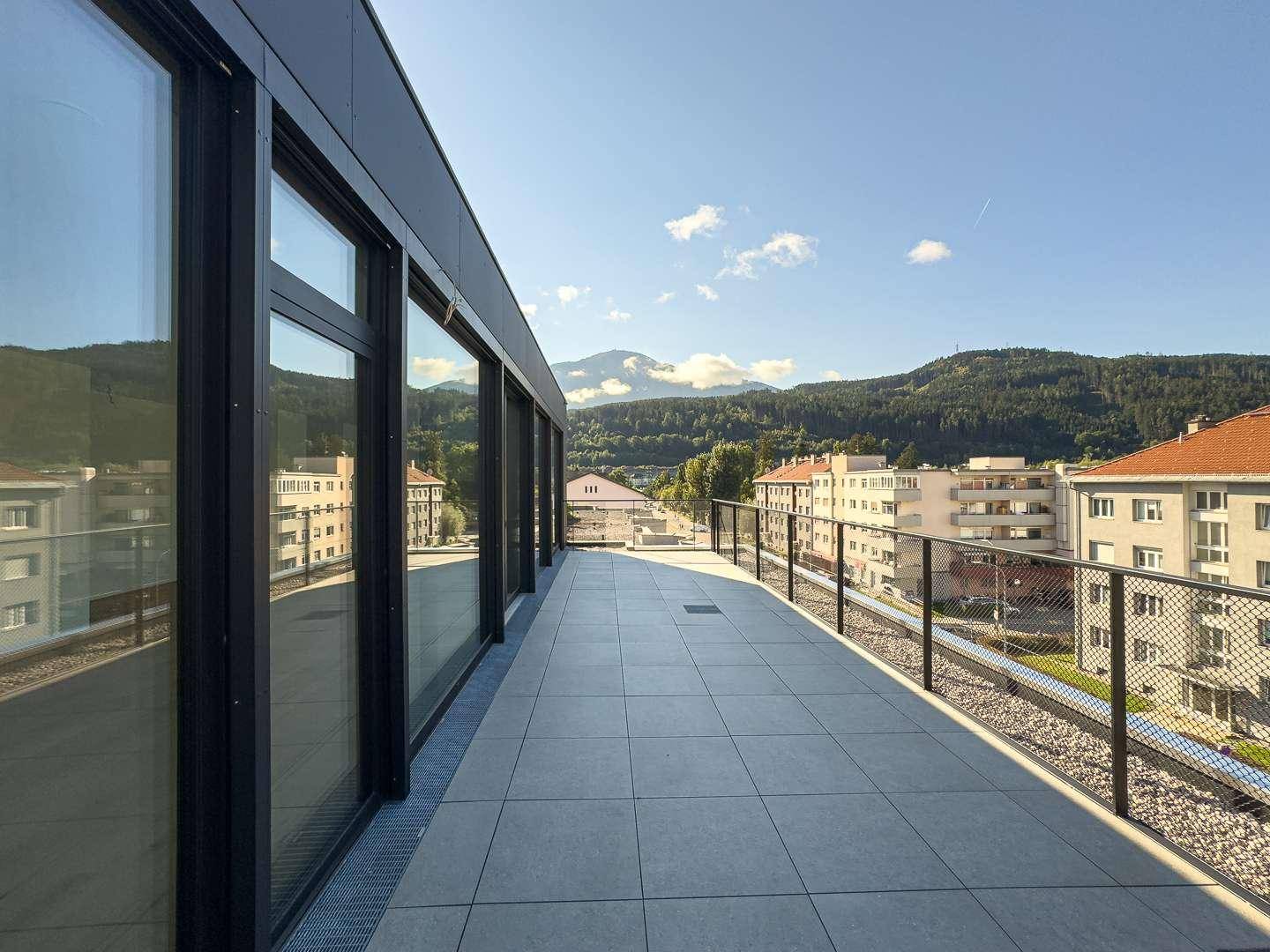 Lange, schmale Terrasse mit Fliesenboden und Blick auf die Stadt und die Berge.
