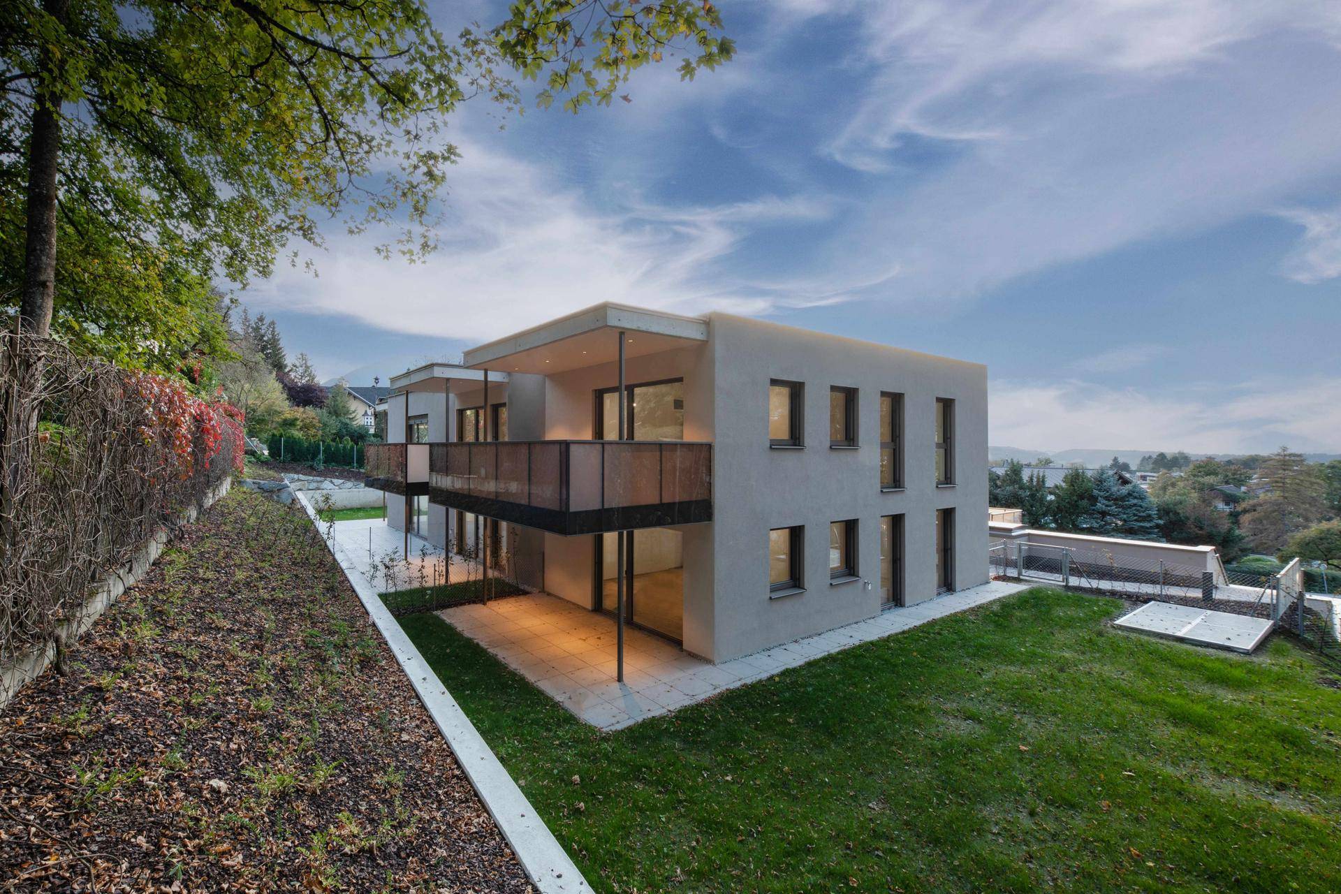Moderne Wohnanlage mit Terrasse, Rasenfläche und herbstlicher Bepflanzung.