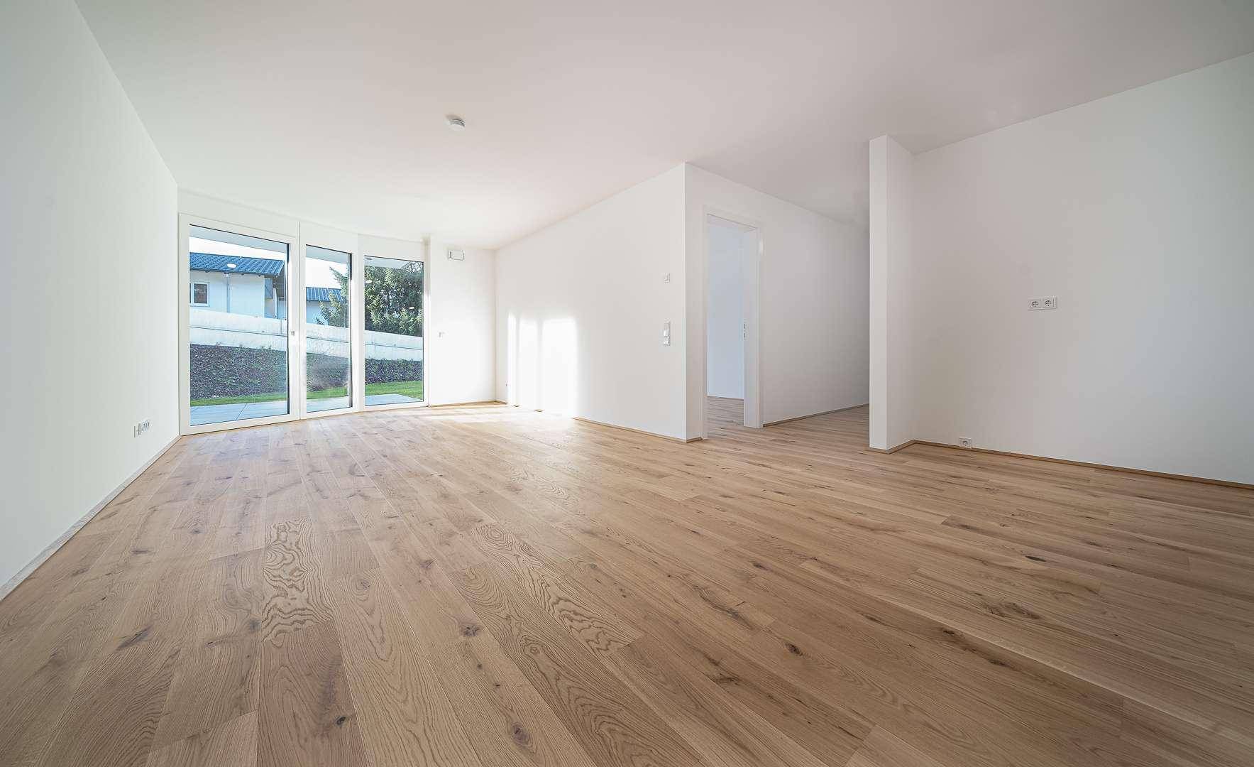 Heller, leerer Wohnbereich mit großen Fenstern und hochwertigem Holzparkettboden.