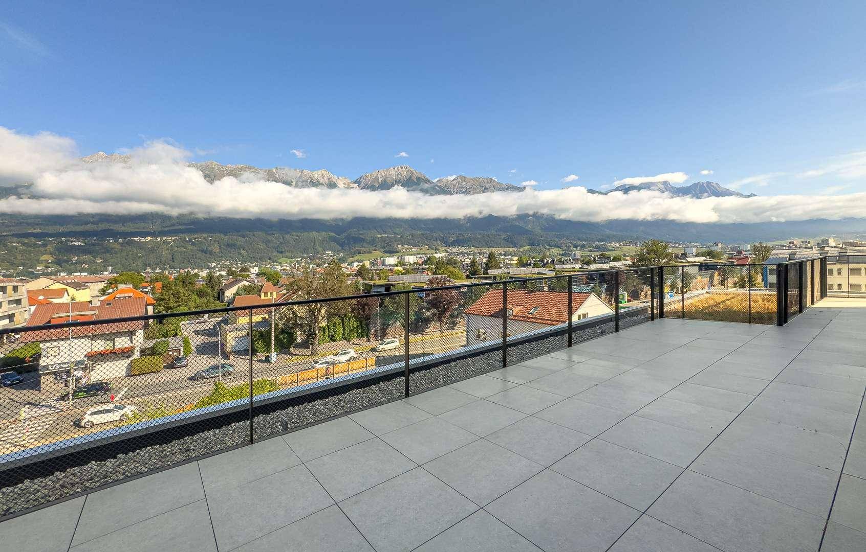 Weitläufige Dachterrasse mit Fliesenboden und atemberaubendem Bergblick unter blauem Himmel.