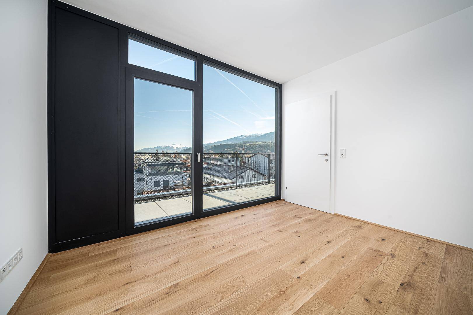 Helles Schlafzimmer mit Holzboden, Einbauschrank und großem Fenster mit Stadt- und Bergblick.