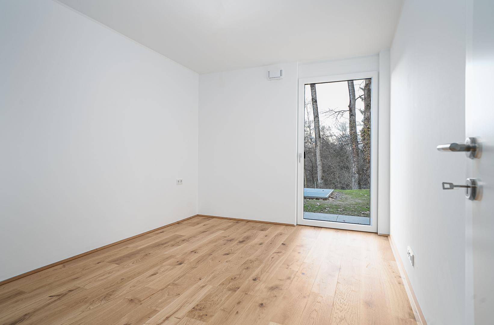 Leeres Zimmer mit Holzboden und Zugang zu einem kleinen Außenbereich.