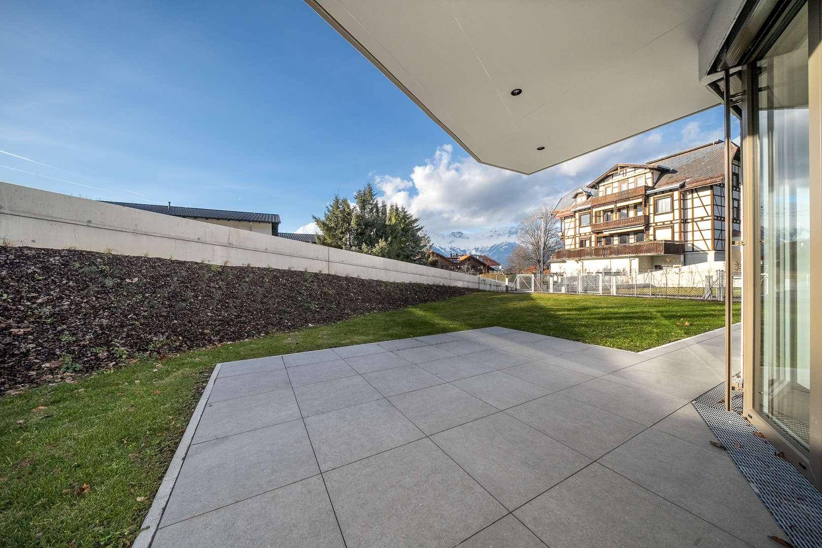 Großzügige Terrasse mit Fliesenboden und angrenzender Rasenfläche, umgeben von Natur.
