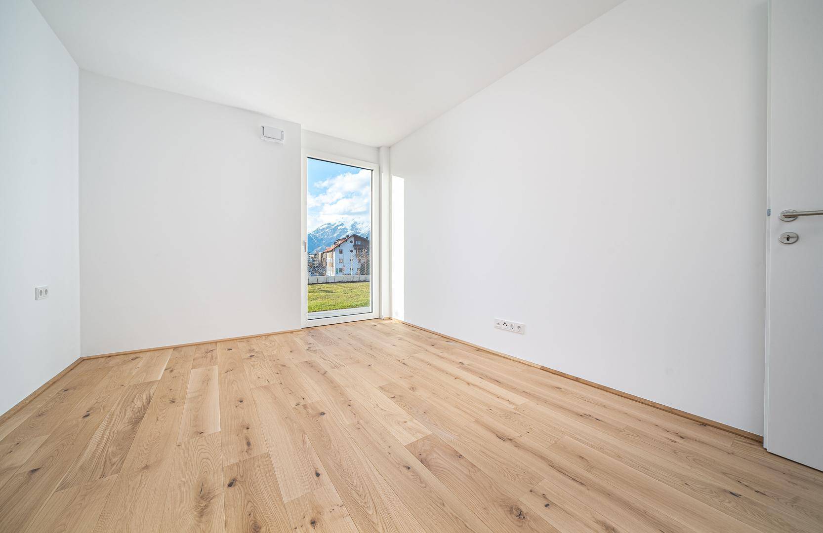 Lichtdurchflutetes Zimmer mit Holzboden und Fenster mit Bergblick, ideal als Schlafzimmer.