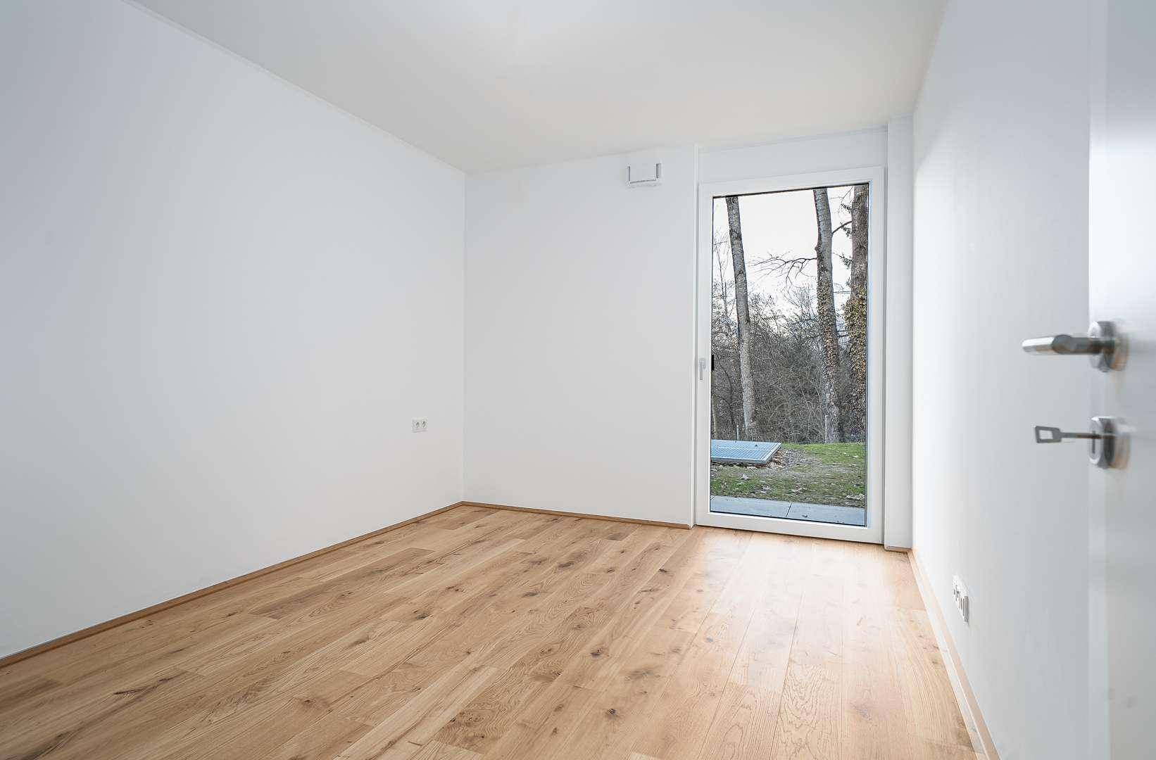 Freundliches Zimmer mit Parkettboden und direktem Zugang zur Grünfläche im Freien.