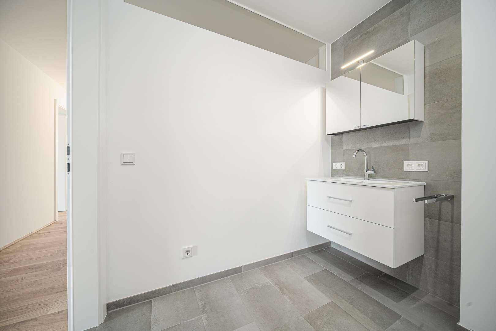 Modernes Badezimmer mit schwebendem Waschtisch, Spiegelschrank und grauen Fliesen.