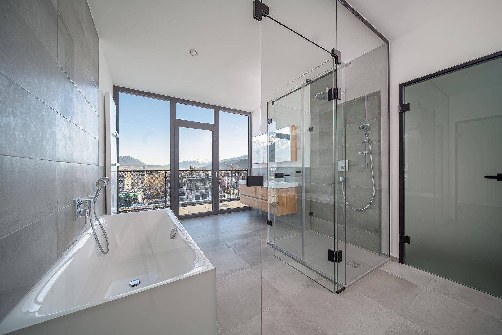 Modernes Badezimmer mit Badewanne, begehbarer Dusche und großen Fenstern mit Bergblick.