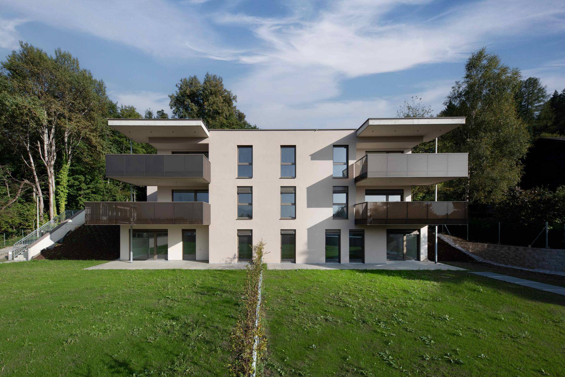 Symmetrische Fassade einer modernen Wohnanlage mit Balkonen und Grünfläche.
