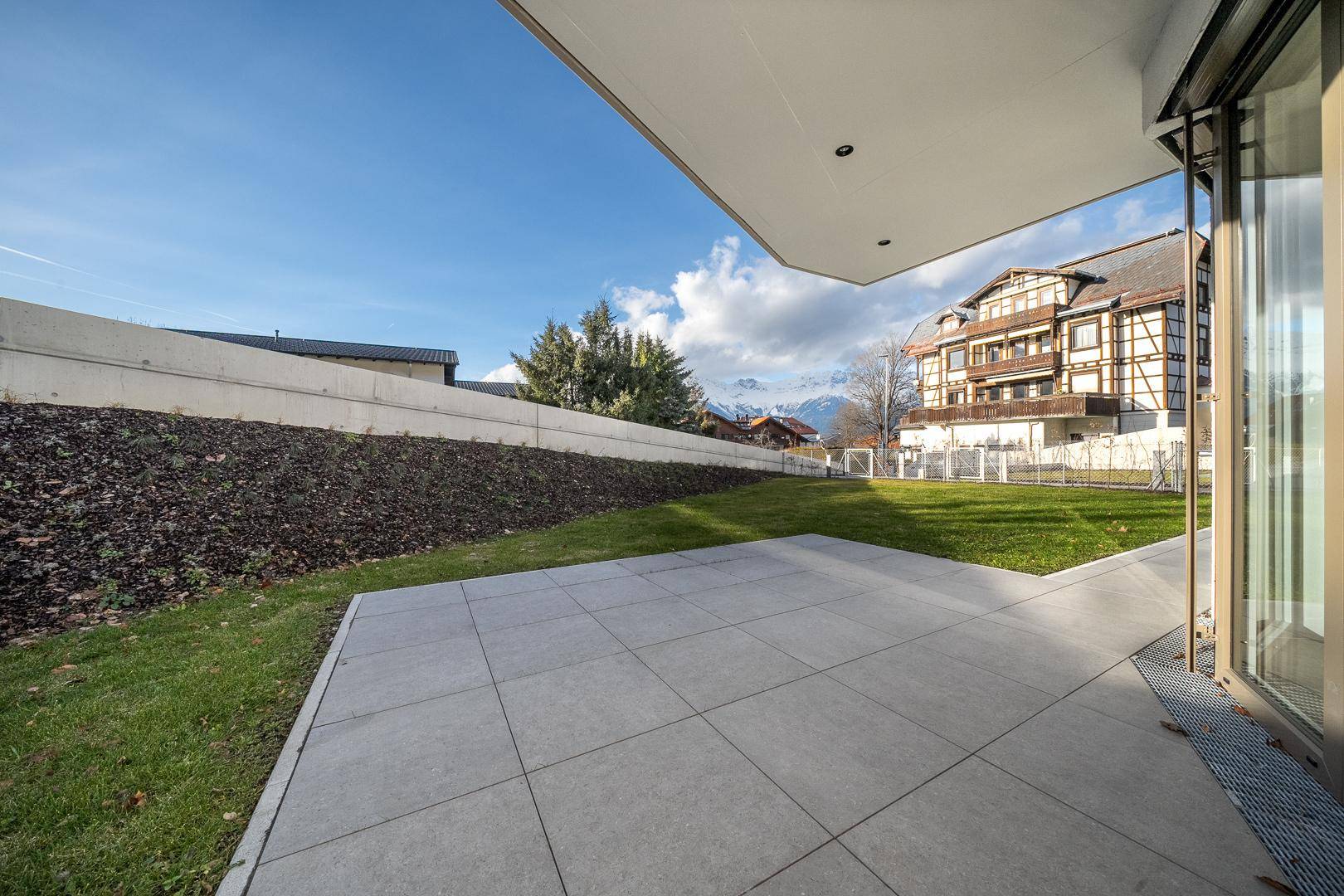 Geräumige Terrasse mit Fliesenboden und angrenzendem Garten, umgeben von Natur und Bergblick.