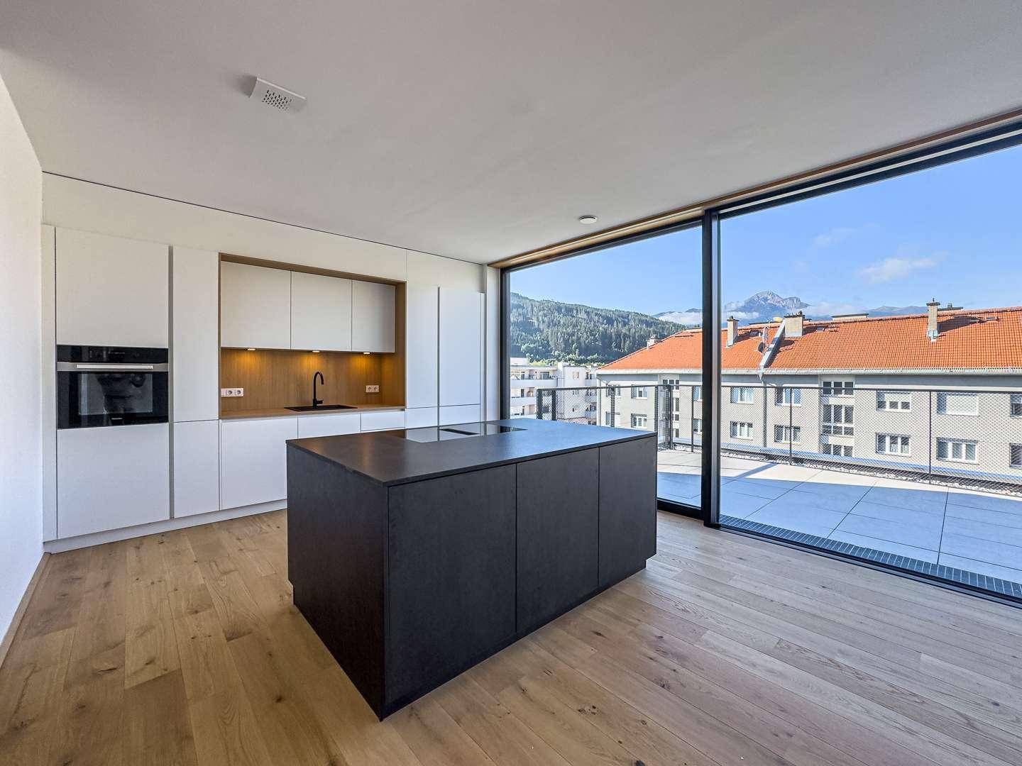 Moderne Küche mit weißer Einbauküche, dunkler Kochinsel und großen Fenstern mit Bergblick.