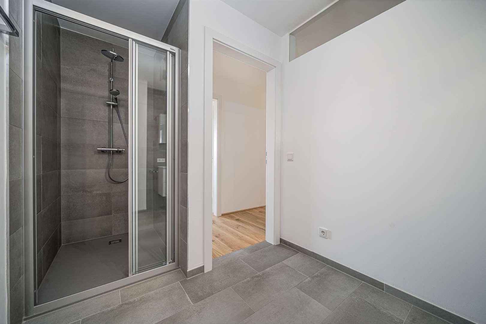 Geräumige Dusche mit Glasabtrennung und modernen grauen Wand- und Bodenfliesen.