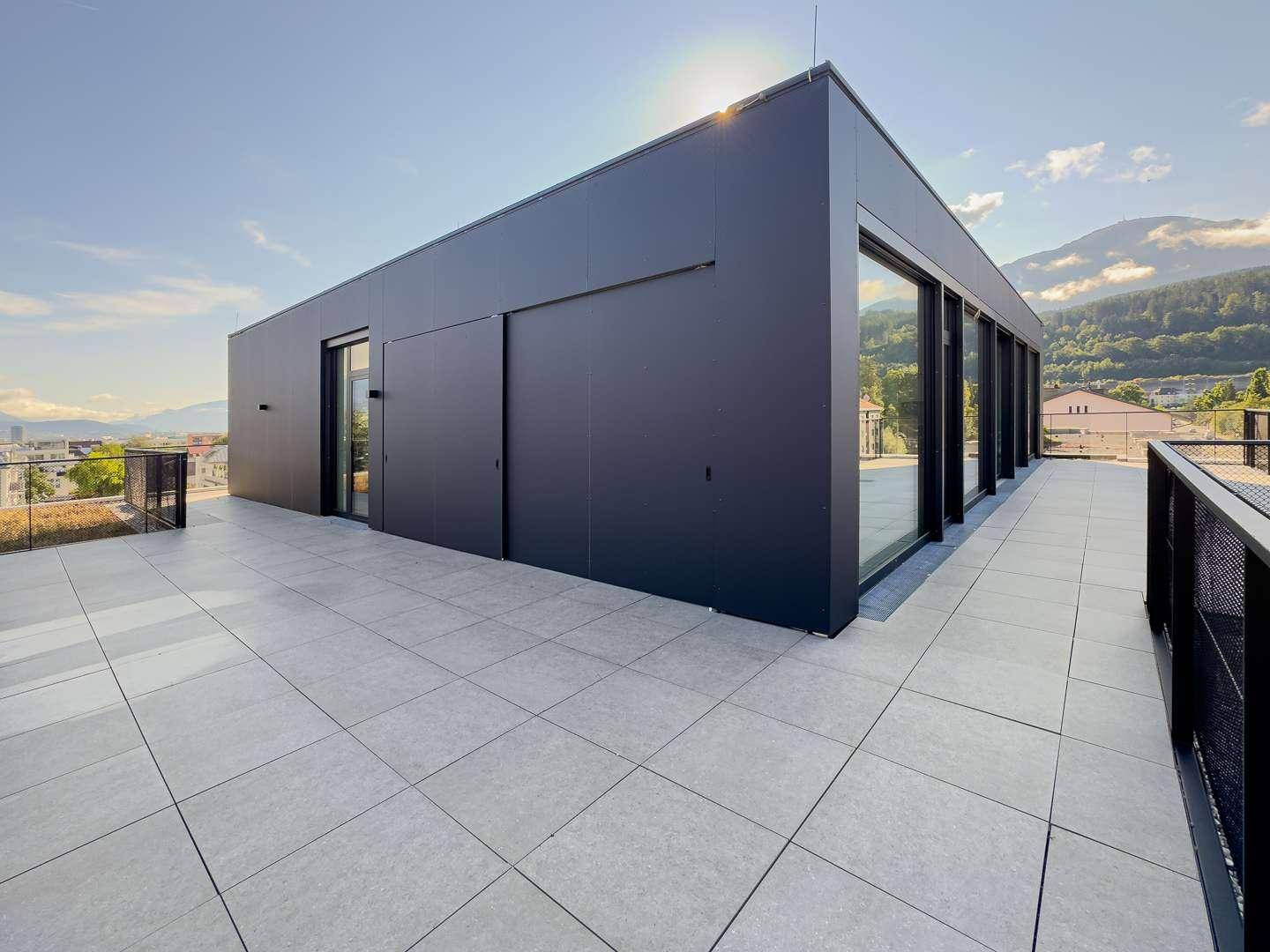 Weitläufige Dachterrasse mit moderner schwarzer Fassade und Blick auf die umliegende Landschaft.