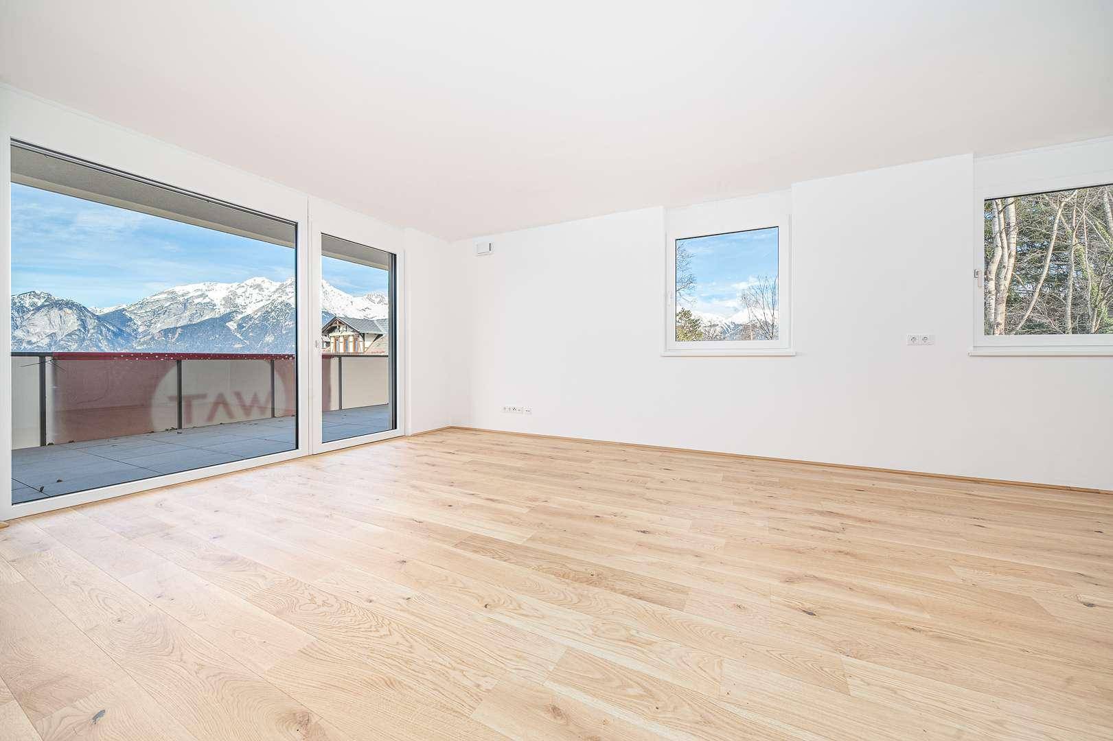 Helles Wohnzimmer mit hellem Holzparkett und großen Fenstern mit Bergblick.