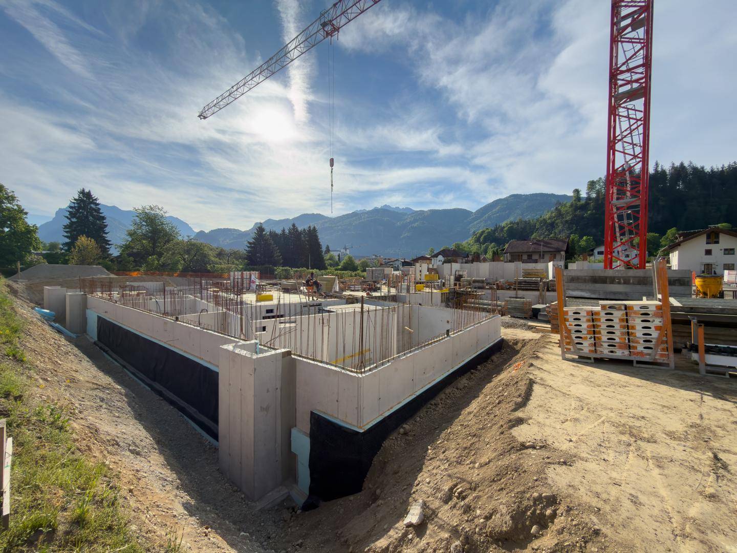 Baustelle eines Neubaus mit Betonfundamenten und Bewehrungsstahl unter einem sonnigen Himmel.