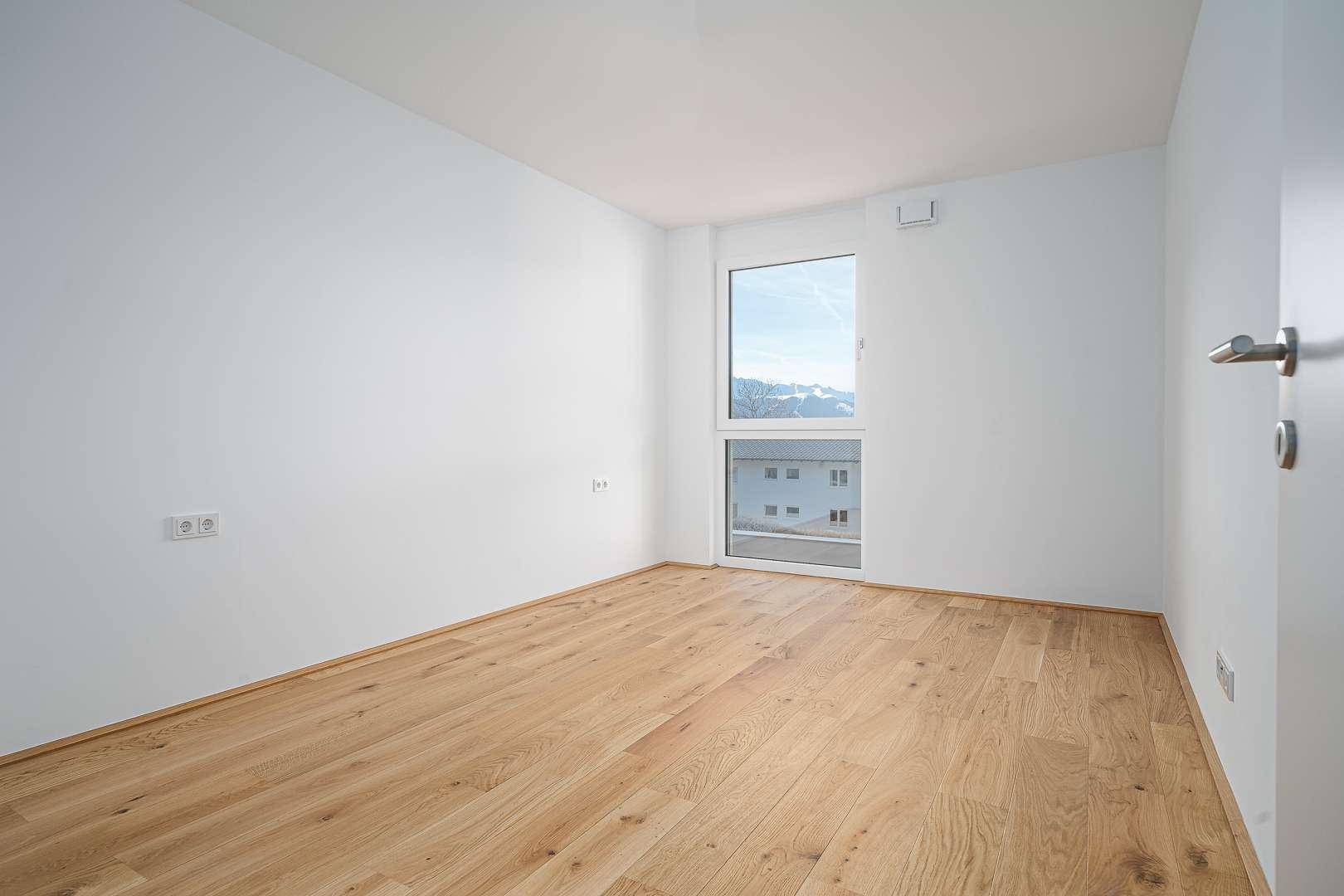 Schlafzimmer mit hellem Eichenparkett und Fenster mit Blick auf die umliegende Bebauung.