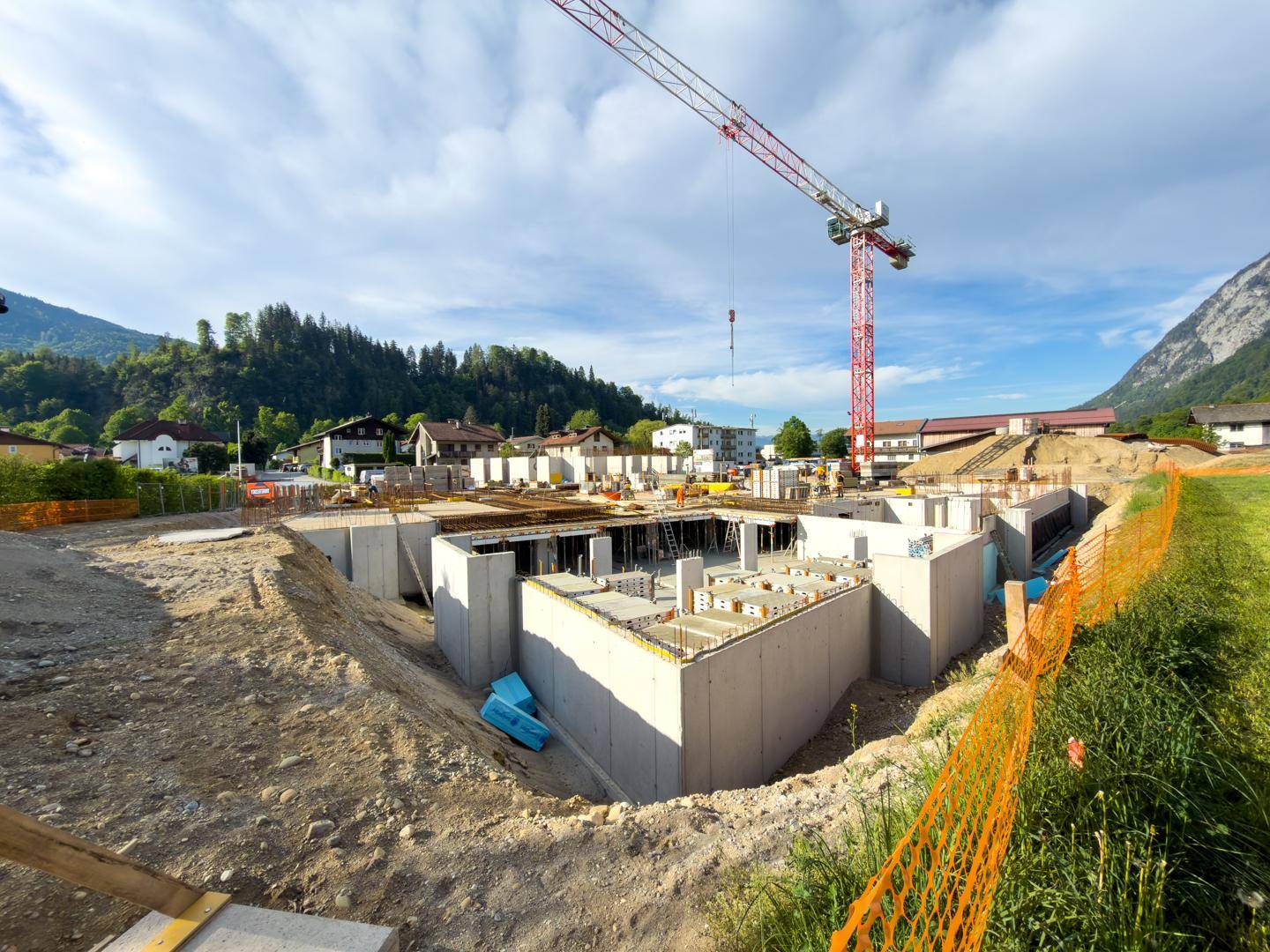 Baustelle mit bereits errichteten Fundamenten und Kellerwänden, umgeben von einer ländlichen Berglandschaft.
