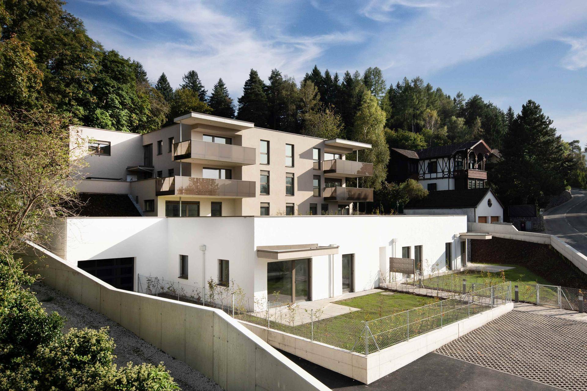Moderne Wohnanlage am Hang mit Terrassen, Balkonen und grüner Umgebung.