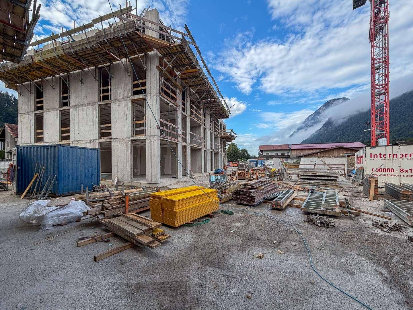 Baustelle eines neuen Wohngebäudes mit Gerüsten und Baumaterialien unter bewölktem Himmel.