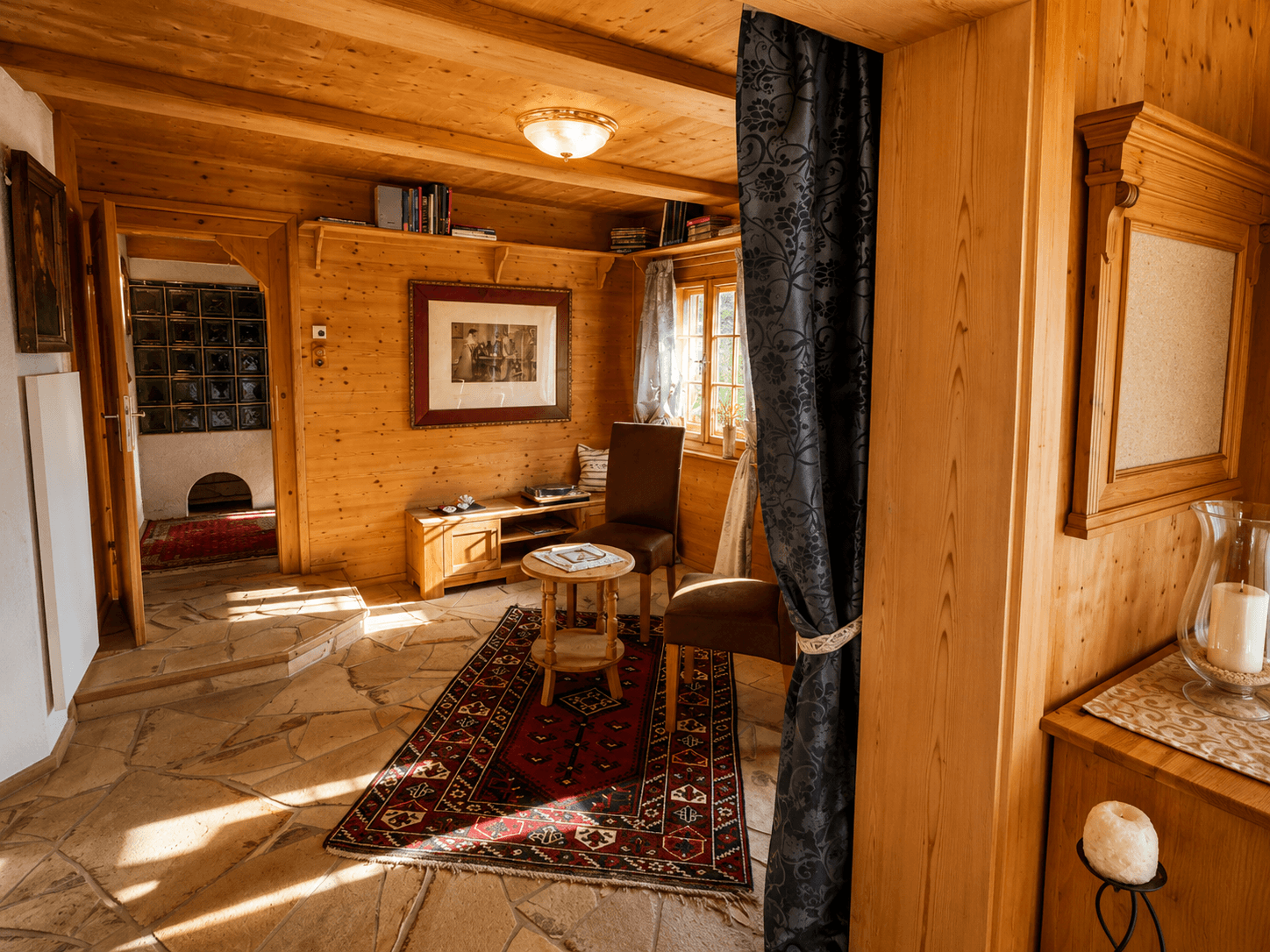 Gemütlicher Wohnbereich mit Holzvertäfelung, Steinboden und traditionellem Teppich.
