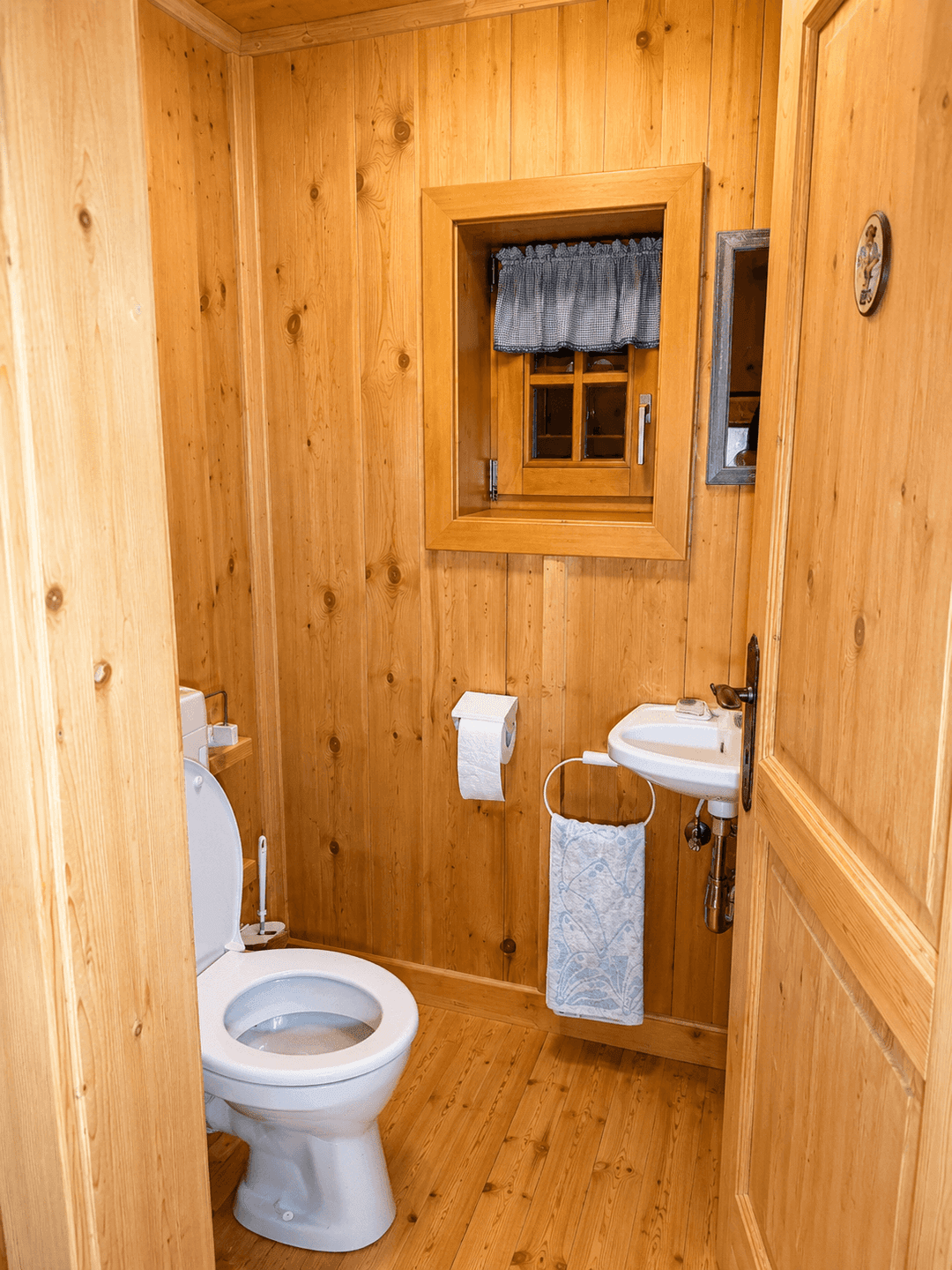 Kleines Gäste-WC mit Holzvertäfelung, Toilette, kleinem Waschbecken und einem Fenster für Belüftung.