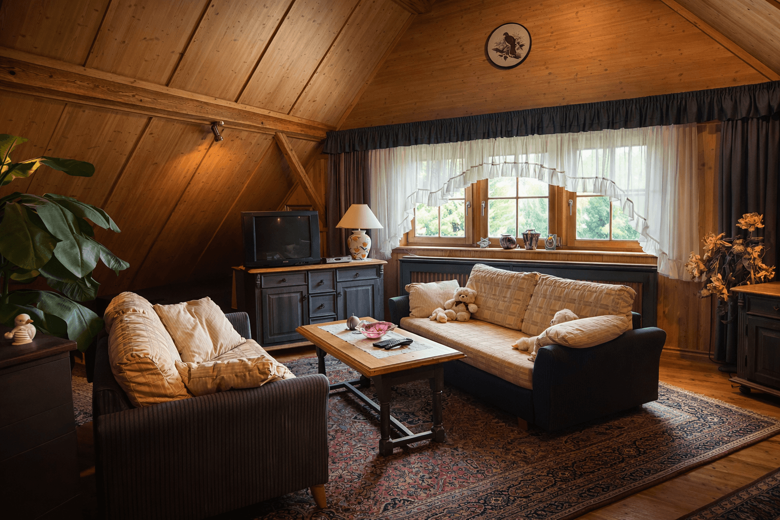 Gemütliches Wohnzimmer im Dachgeschoss mit Holztäfelung, Sofas und Fernseher.