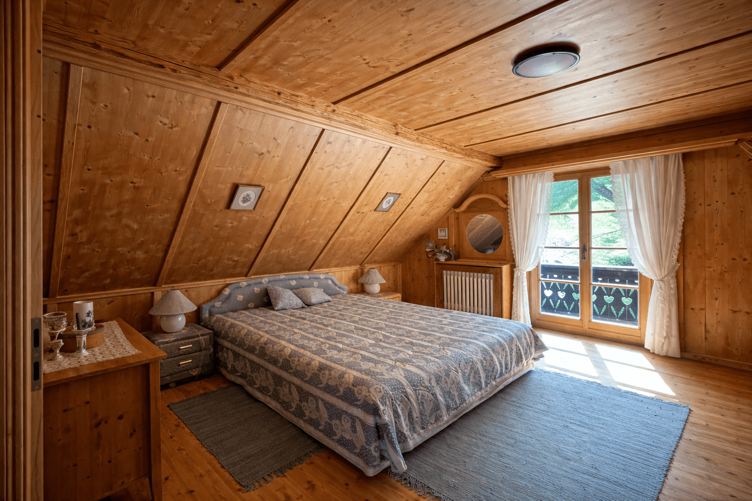 Schlafzimmer mit Holztäfelung, Holzbalkendecke und Zugang zu einem kleinen Balkon.