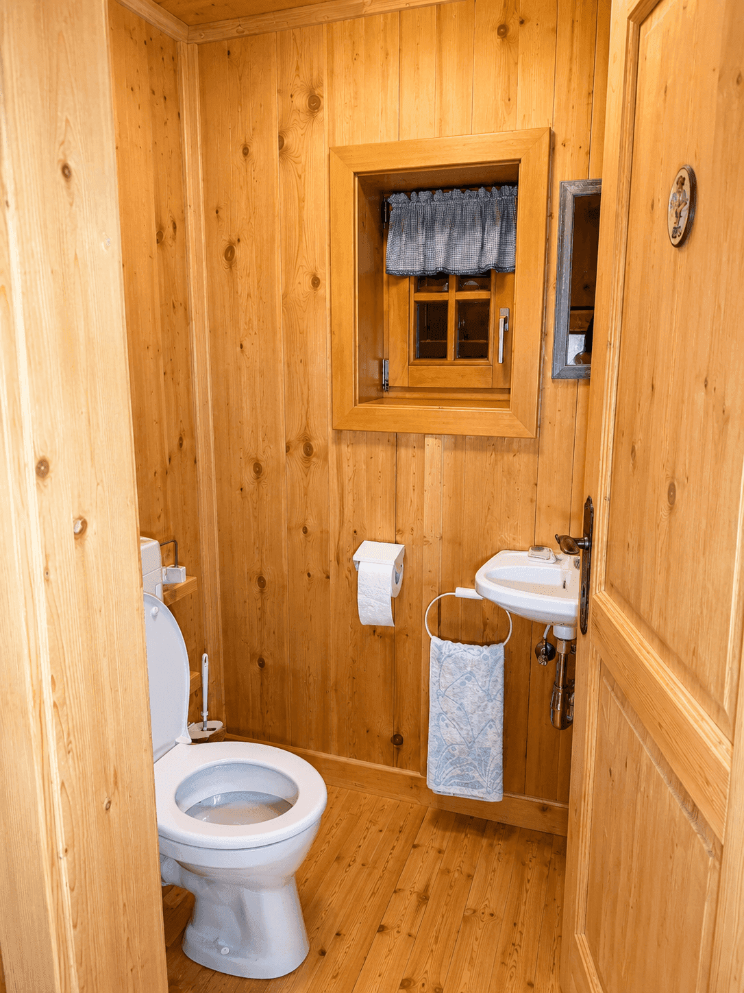 Gemütliches Gäste-WC mit Holzvertäfelung, Toilette und kleinem Handwaschbecken.