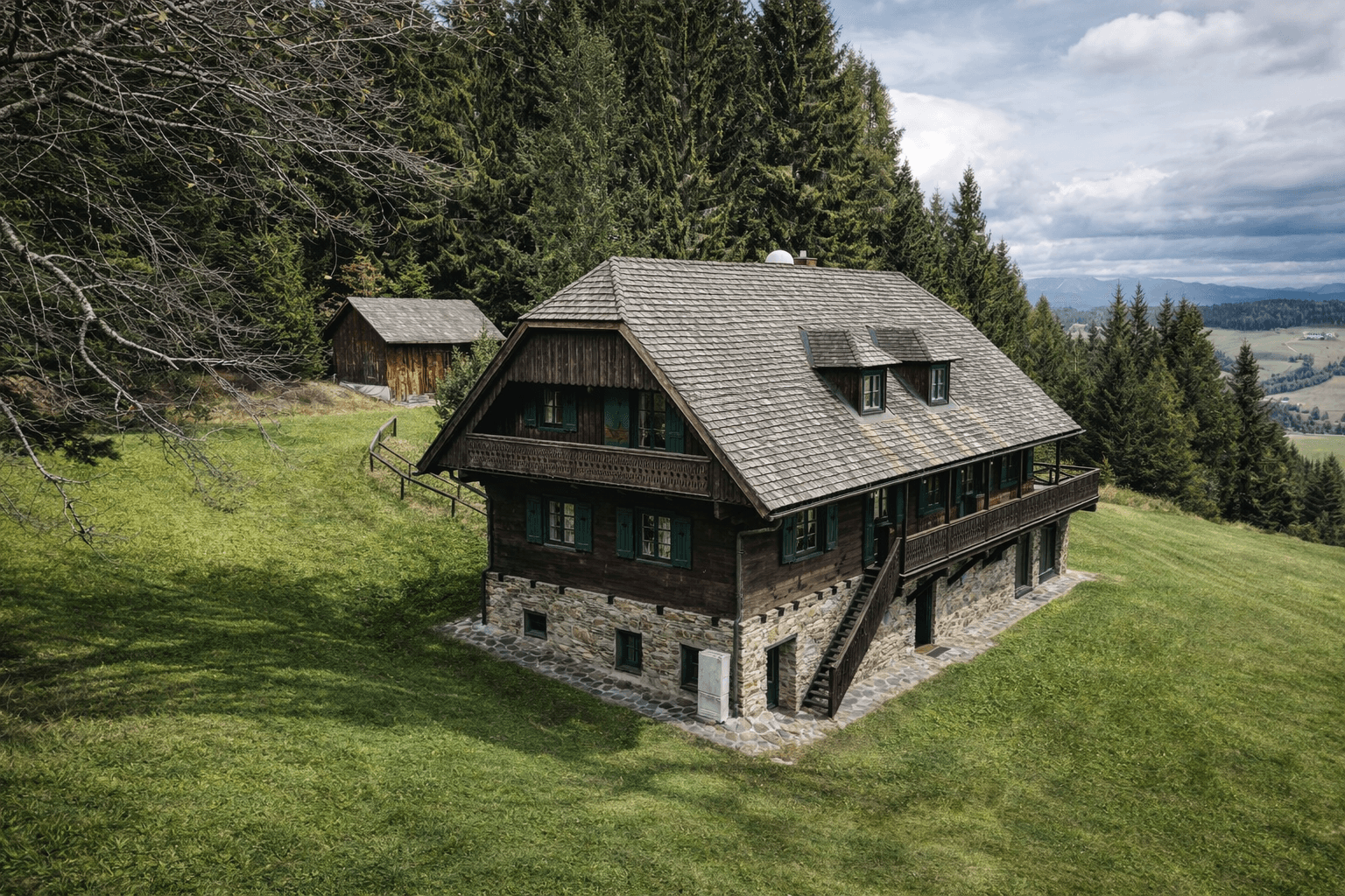 Traditionelles Holzhaus mit Steinfundament und einem Nebengebäude, eingebettet in eine Waldlichtung.