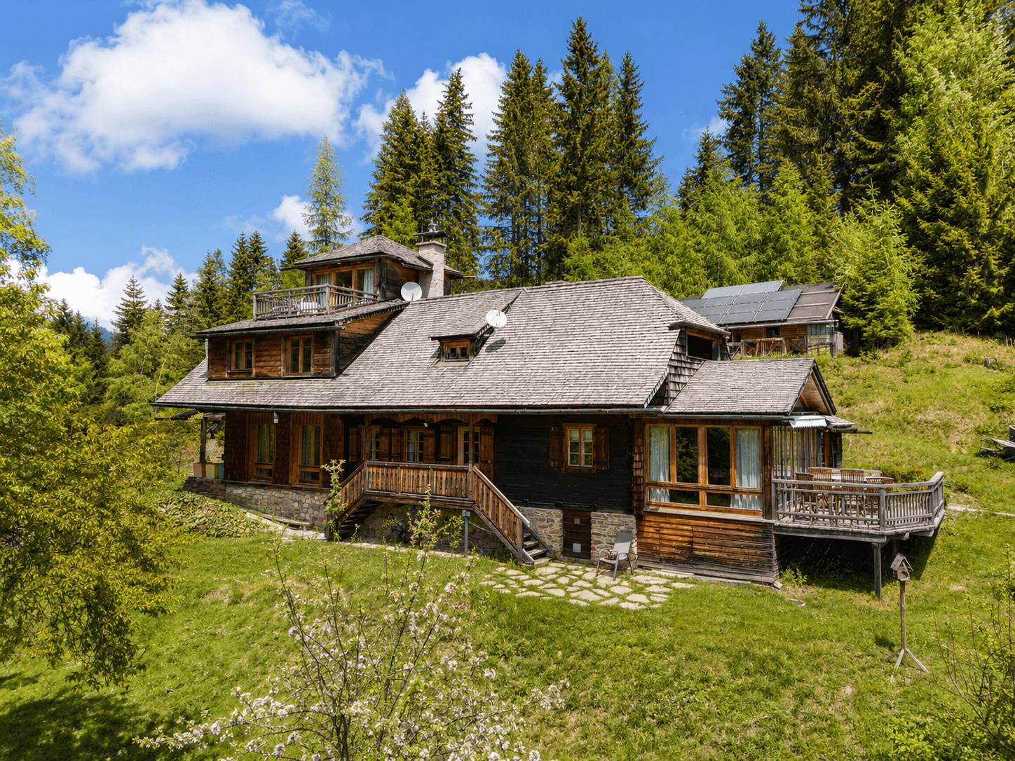 Rustikales Holzhaus mit traditioneller Architektur, umgeben von Wald und mit Solaranlage auf dem Dach.