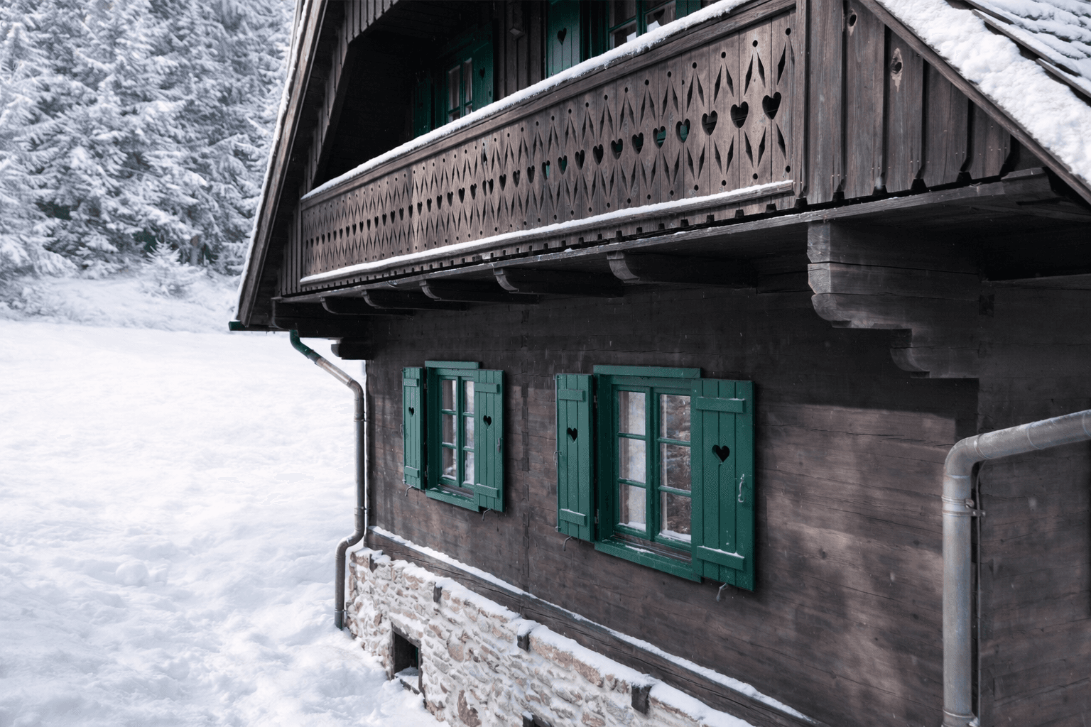 Detailansicht der Holzfassade mit grünen Fensterläden und herzförmigen Ausschnitten im Winter.