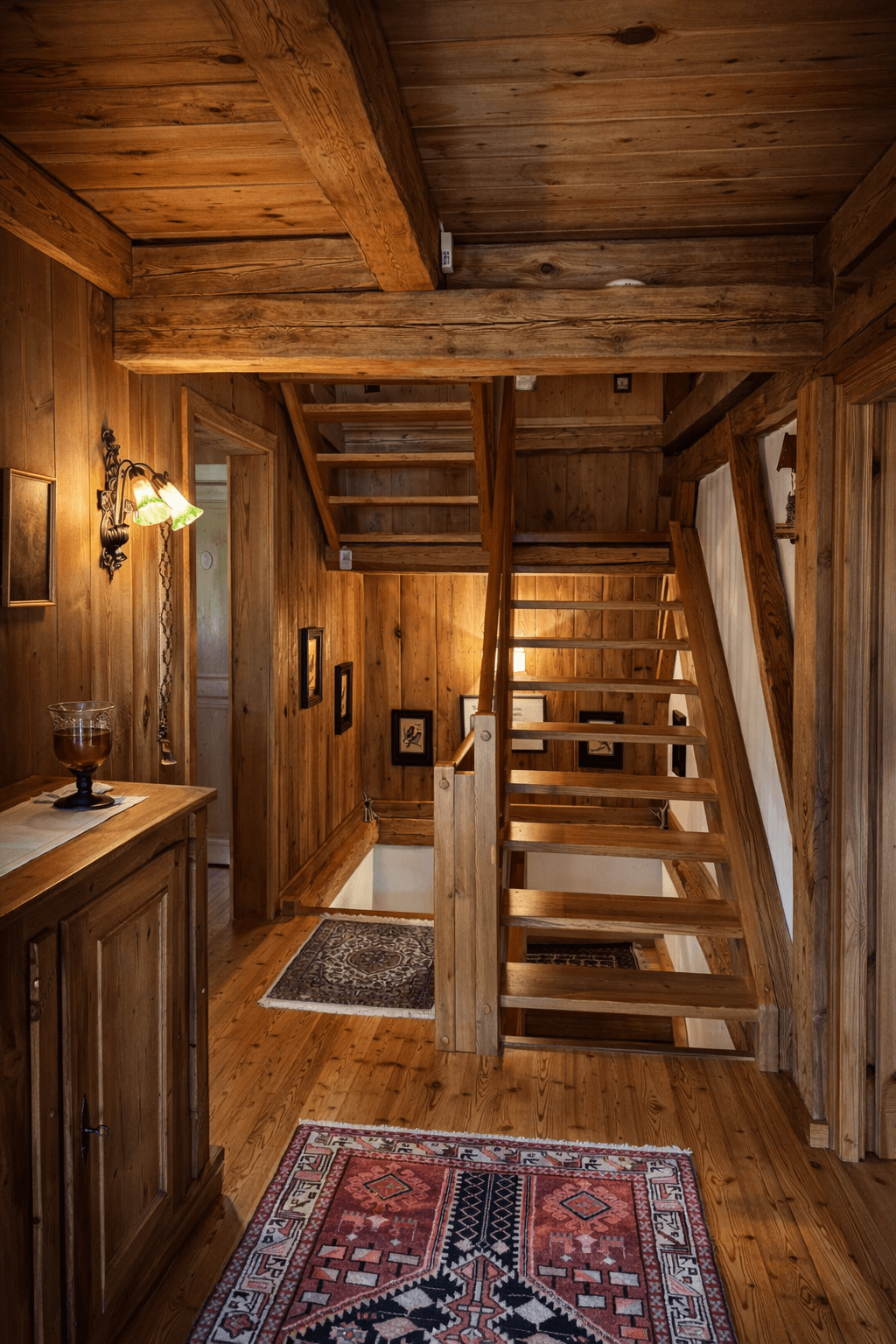 Rustikaler Treppenaufgang aus Holz mit Holzbalkendecke und traditionellen Teppichen.