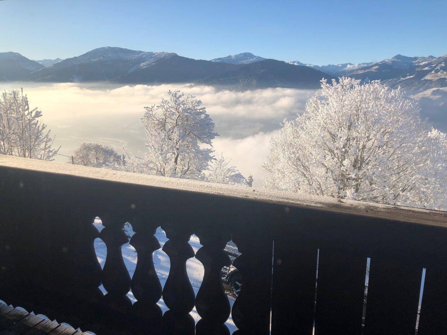Winterlicher Ausblick von einem Balkon über eine Nebeldecke und verschneite Berge.