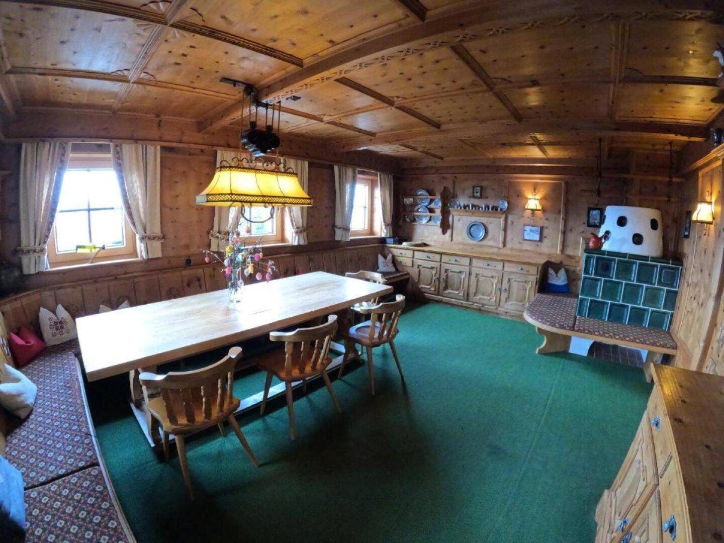 Gemütlicher Essbereich im alpinen Stil mit Holztäfelung, Kachelofen und grüner Auslegware.