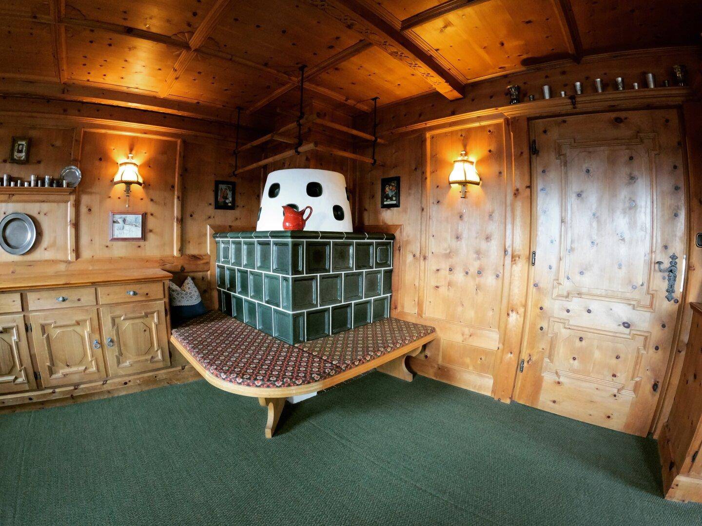 Detailansicht eines traditionellen grünen Kachelofens mit integrierter Sitzbank in einem Holzraum.