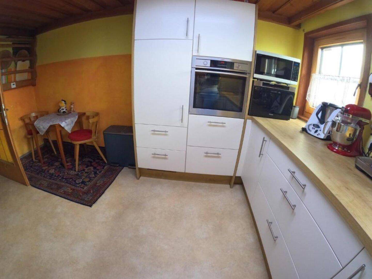 Moderne Einbauküche mit weißen Fronten, integriertem Backofen und kleinem Essbereich.