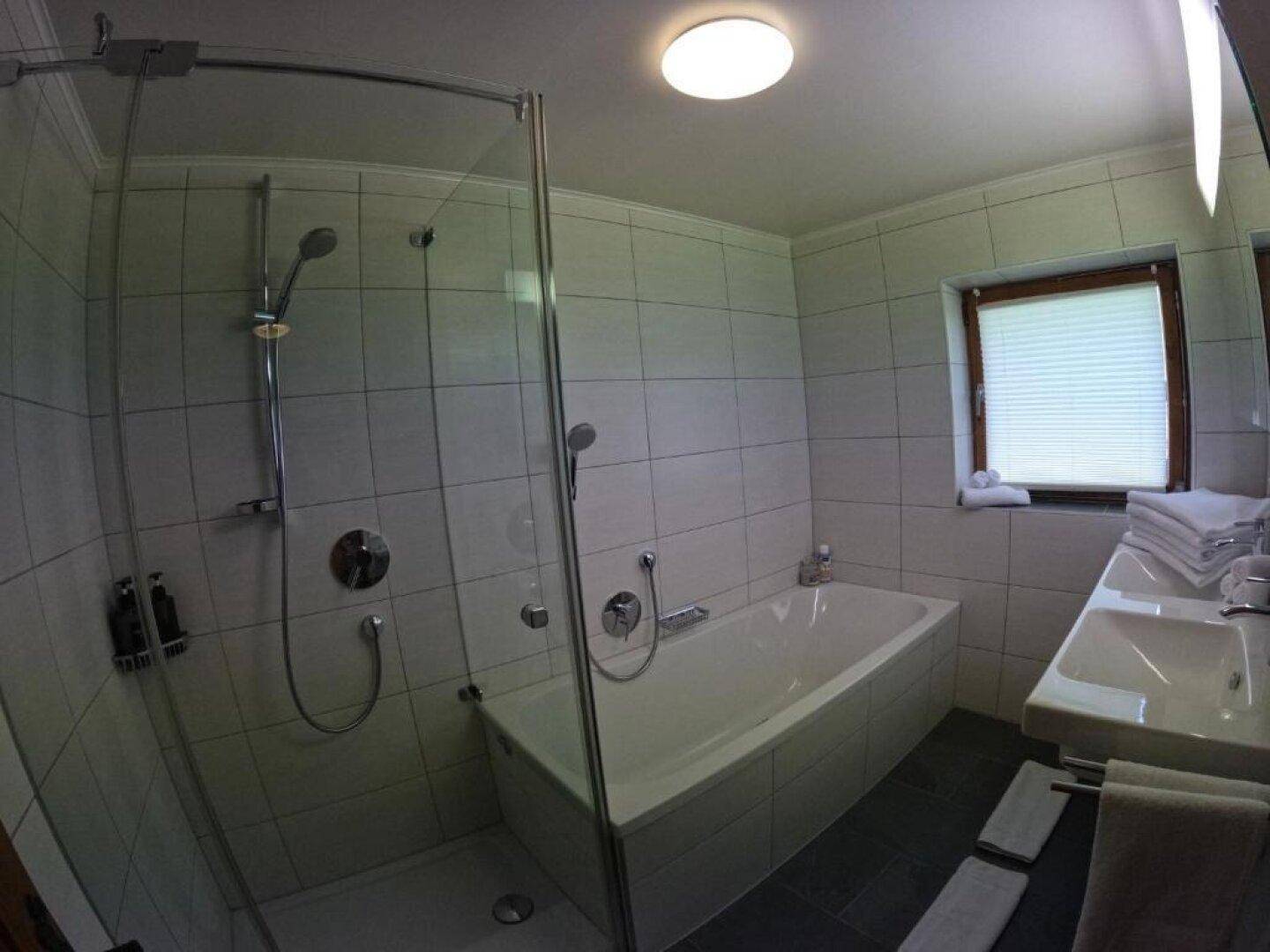 Modernes Badezimmer mit Badewanne, Dusche und Fenster, hell gefliest.