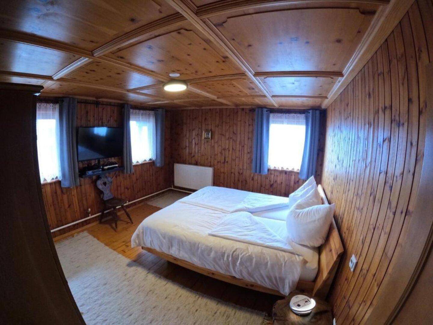 Schlafzimmer im Landhausstil mit Holzwänden, Deckenpaneelen und zwei Fenstern.
