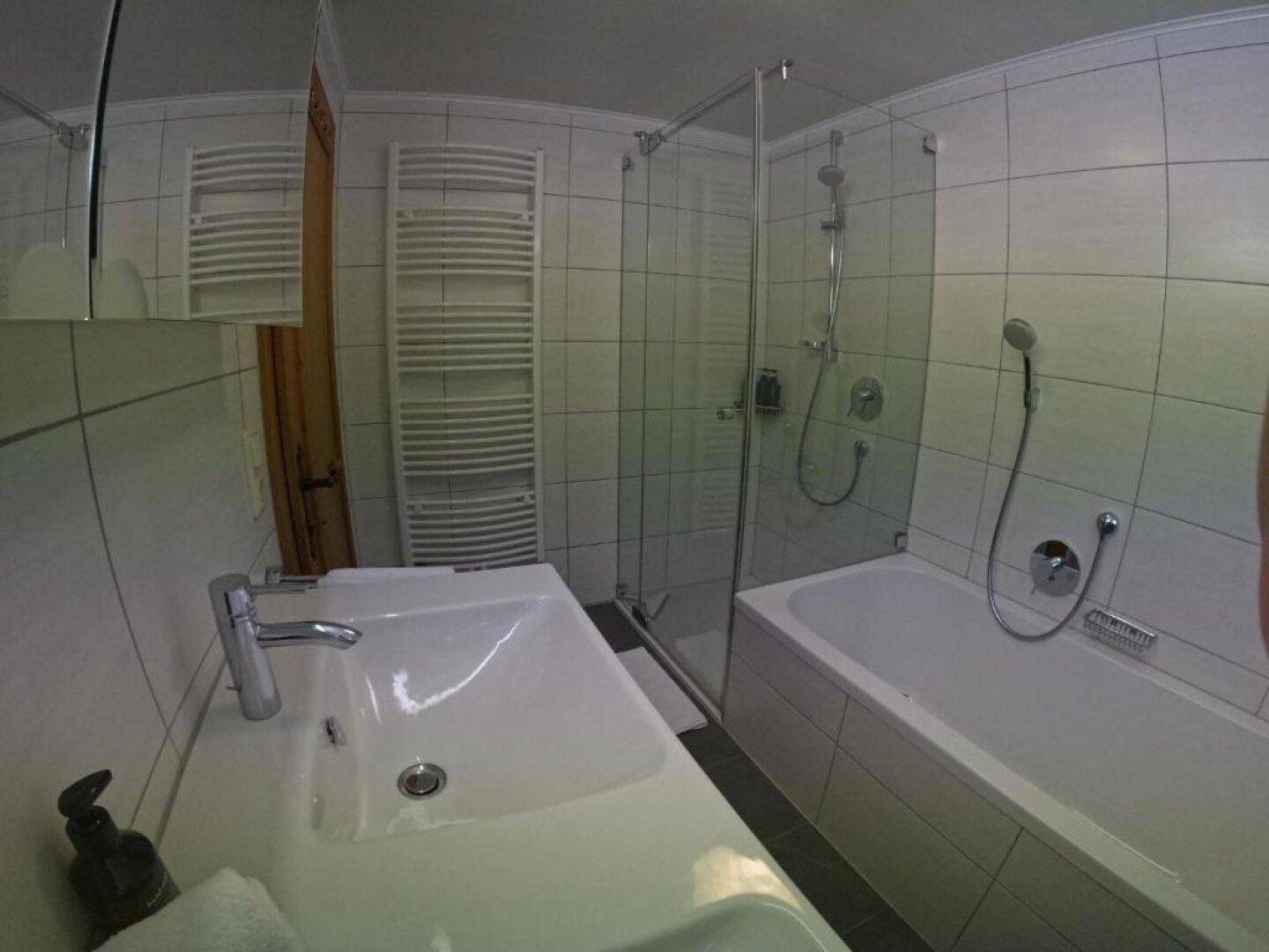 Helles Badezimmer mit Doppelwaschbecken, Dusche, Badewanne und beheiztem Handtuchhalter.