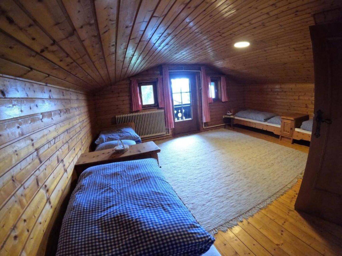 Dachgeschoss-Schlafzimmer mit Holztäfelung, Holzboden und mehreren Einzelbetten.