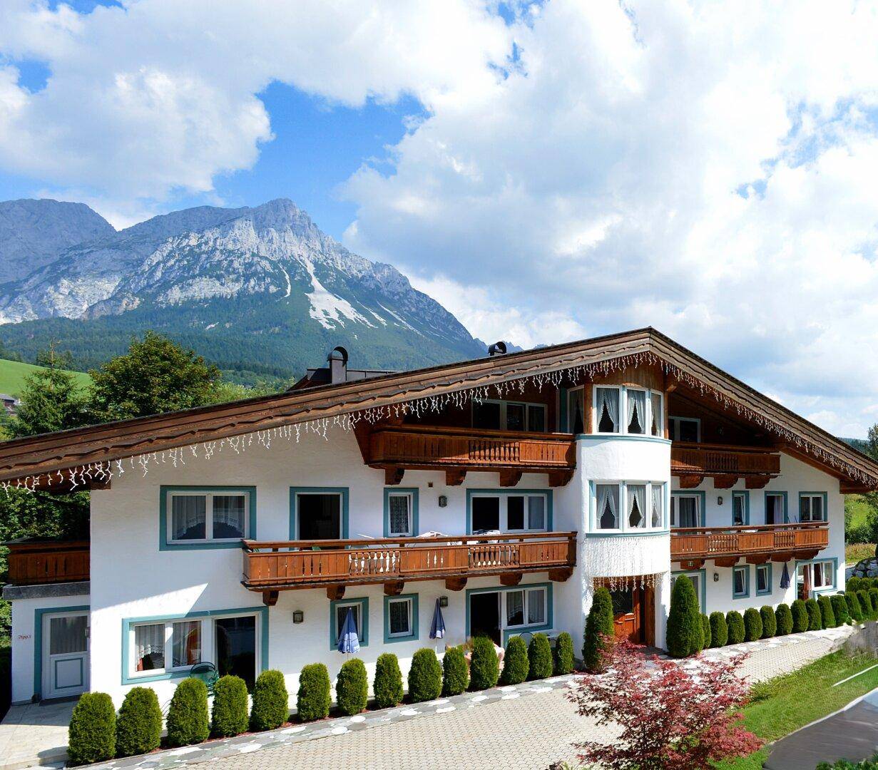 Alpines Gebäude mit Holzbalkonen und gepflegter Bepflanzung unter blauem Himmel.