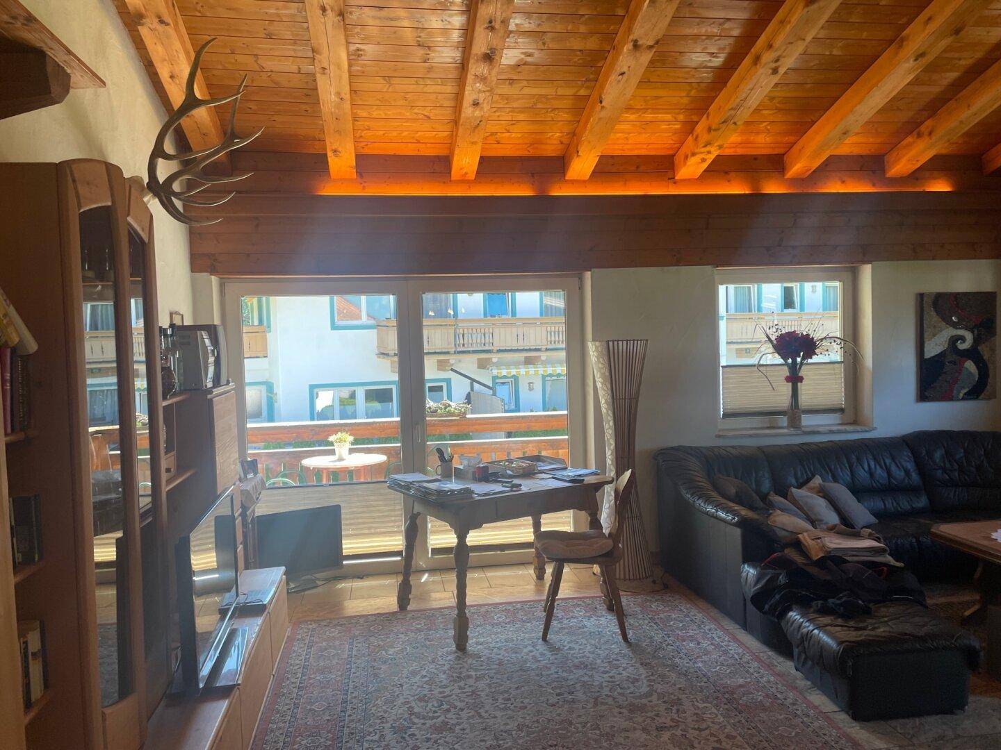 Gemütliches Wohnzimmer im alpinen Stil mit Holzbalkendecke und Blick auf den Balkon.
