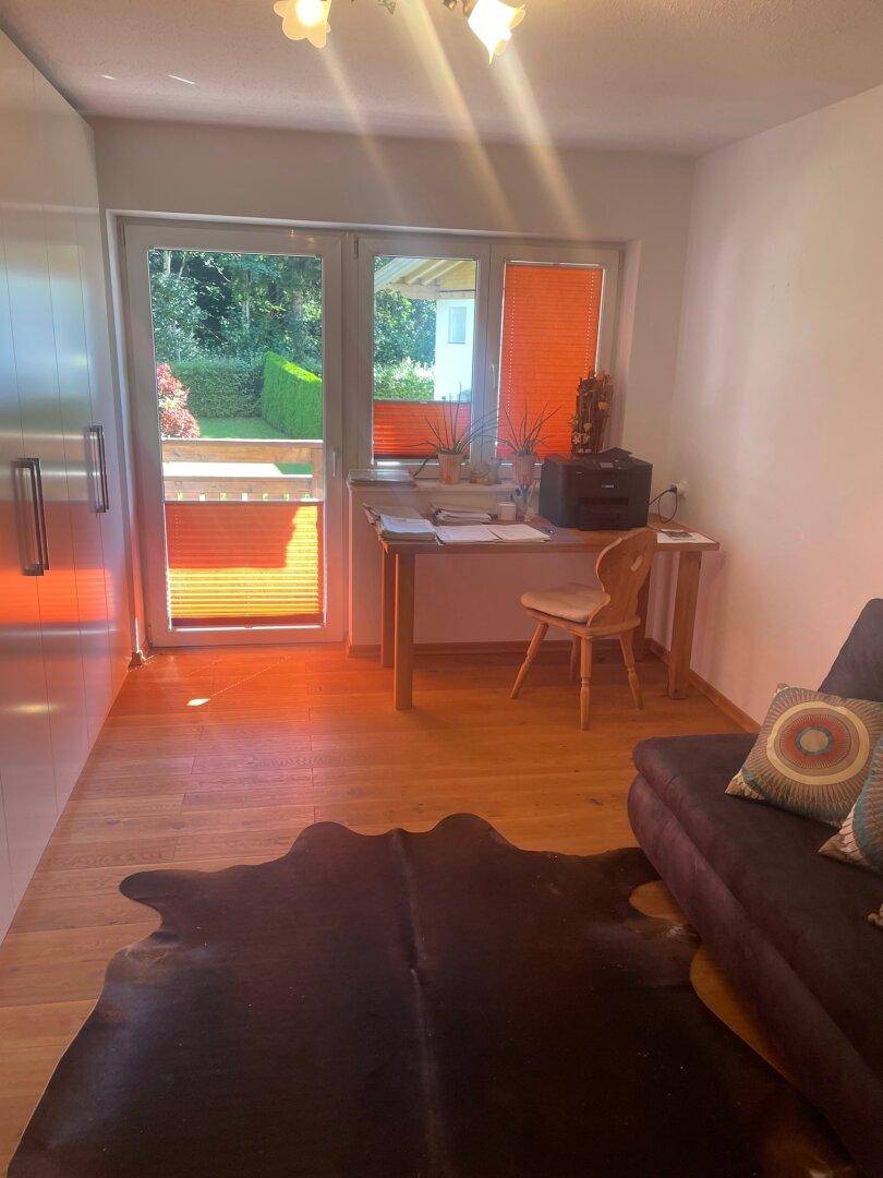 Heller Wohnbereich mit Holzboden, Schreibtisch und Zugang zum Außenbereich.