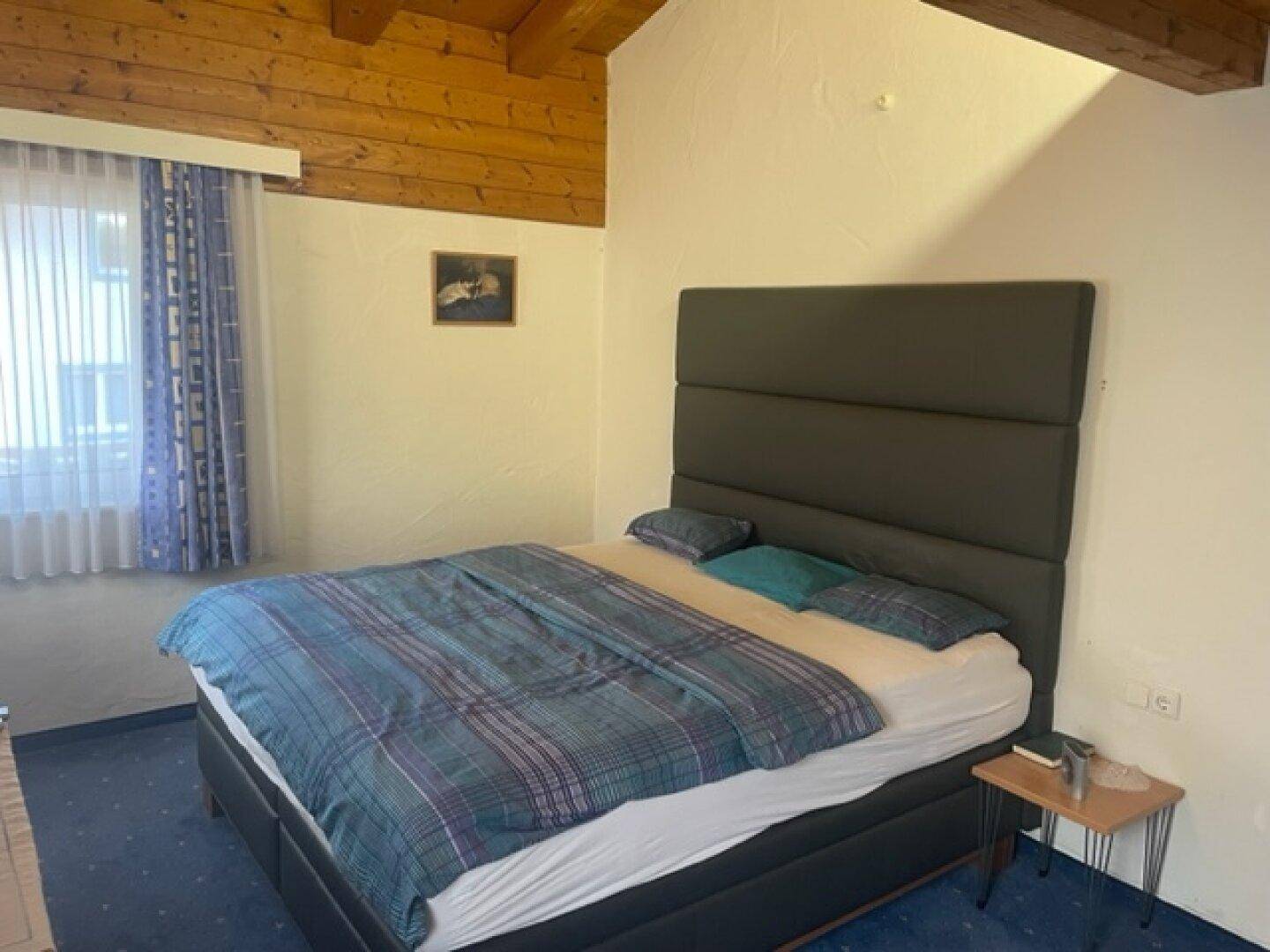 Schlafzimmer mit Doppelbett, Holzbalkendecke und Teppichboden.