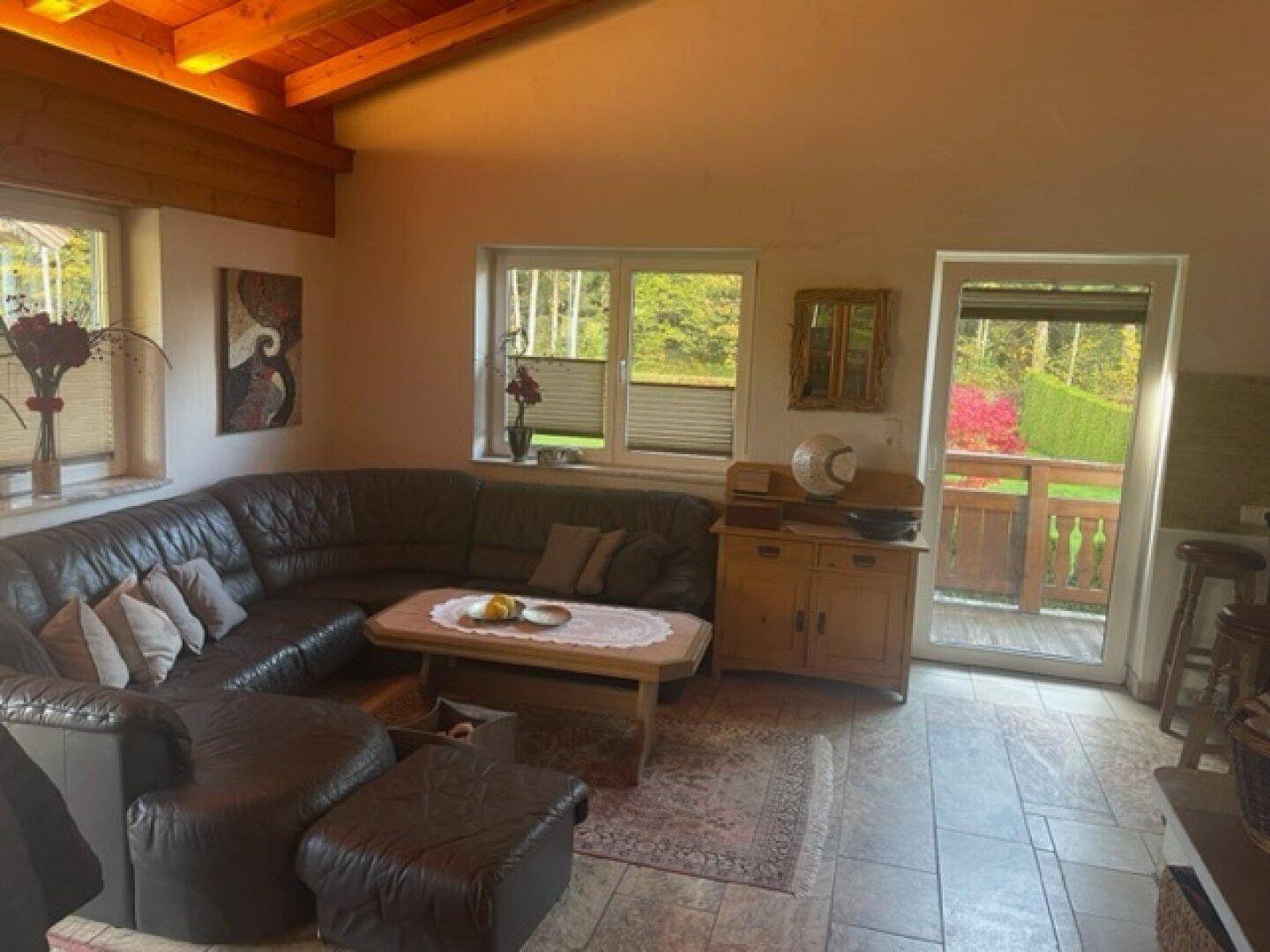 Wohnzimmer mit Ledersofa, Fliesenboden und Zugang zu einem Balkon.