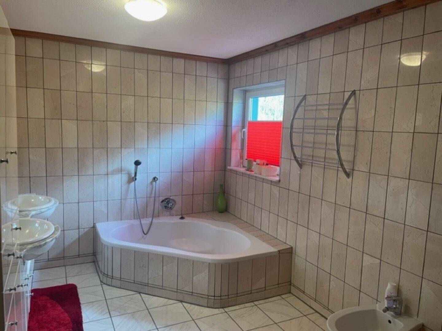 Badezimmer mit Eckbadewanne, Fliesen und Fenster.