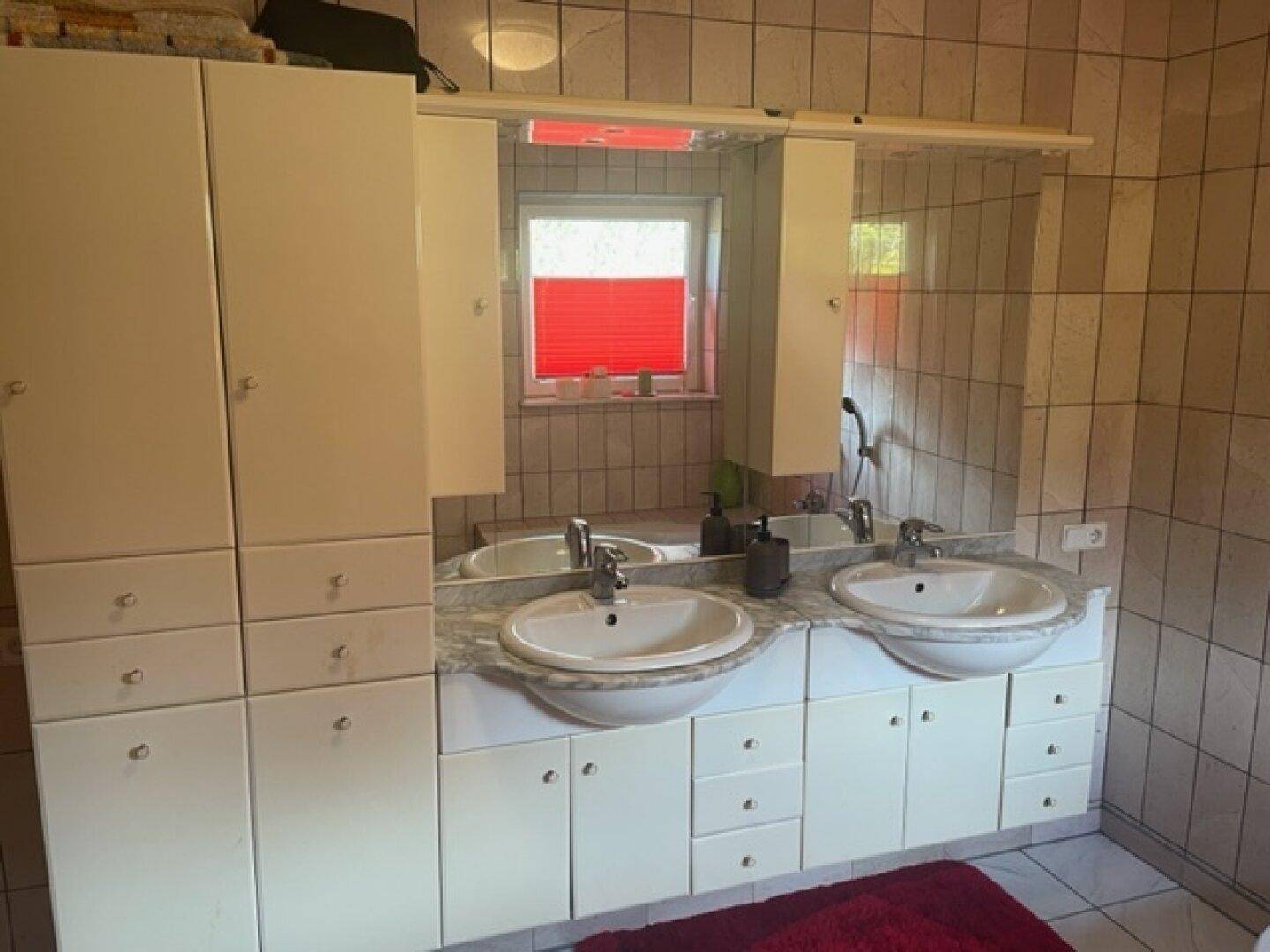 Badezimmer mit Doppelwaschbecken, Spiegelschrank und Fliesen.