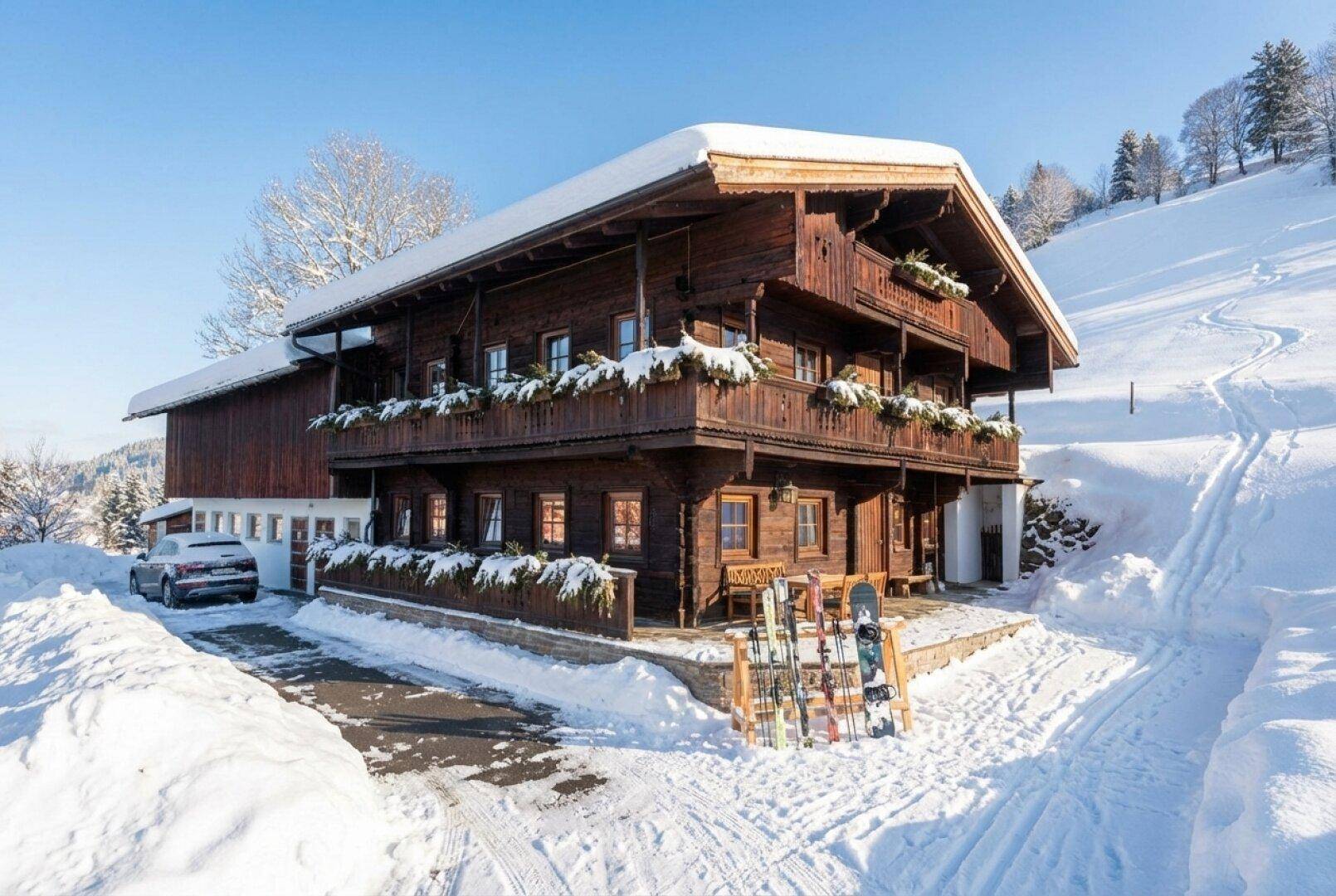 Traditionelles Holzhaus im Schnee mit Skiern und Winterlandschaft, umgeben von verschneiten Hängen.