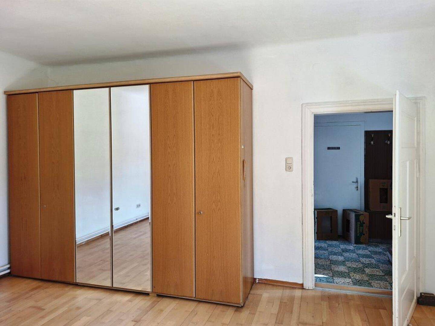 Geräumiger Raum mit großem Holzschrank und Spiegeltüren, ideal als Schlafzimmer oder Ankleide.