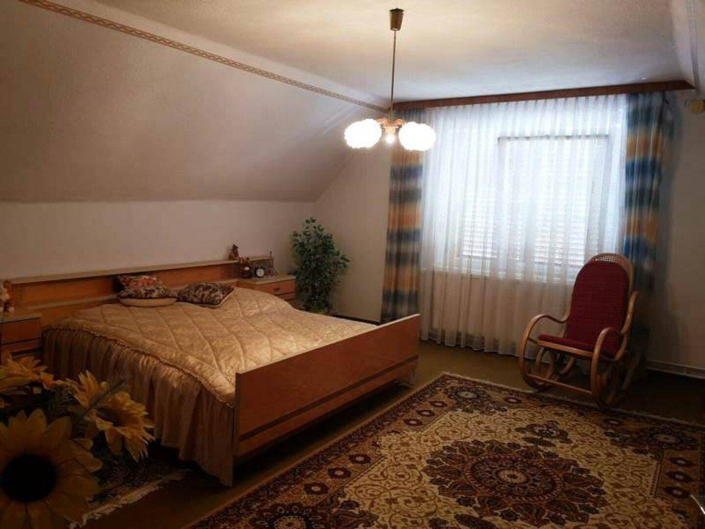 Traditionelles Schlafzimmer mit großem Bett, Schaukelstuhl und gemustertem Teppichboden.